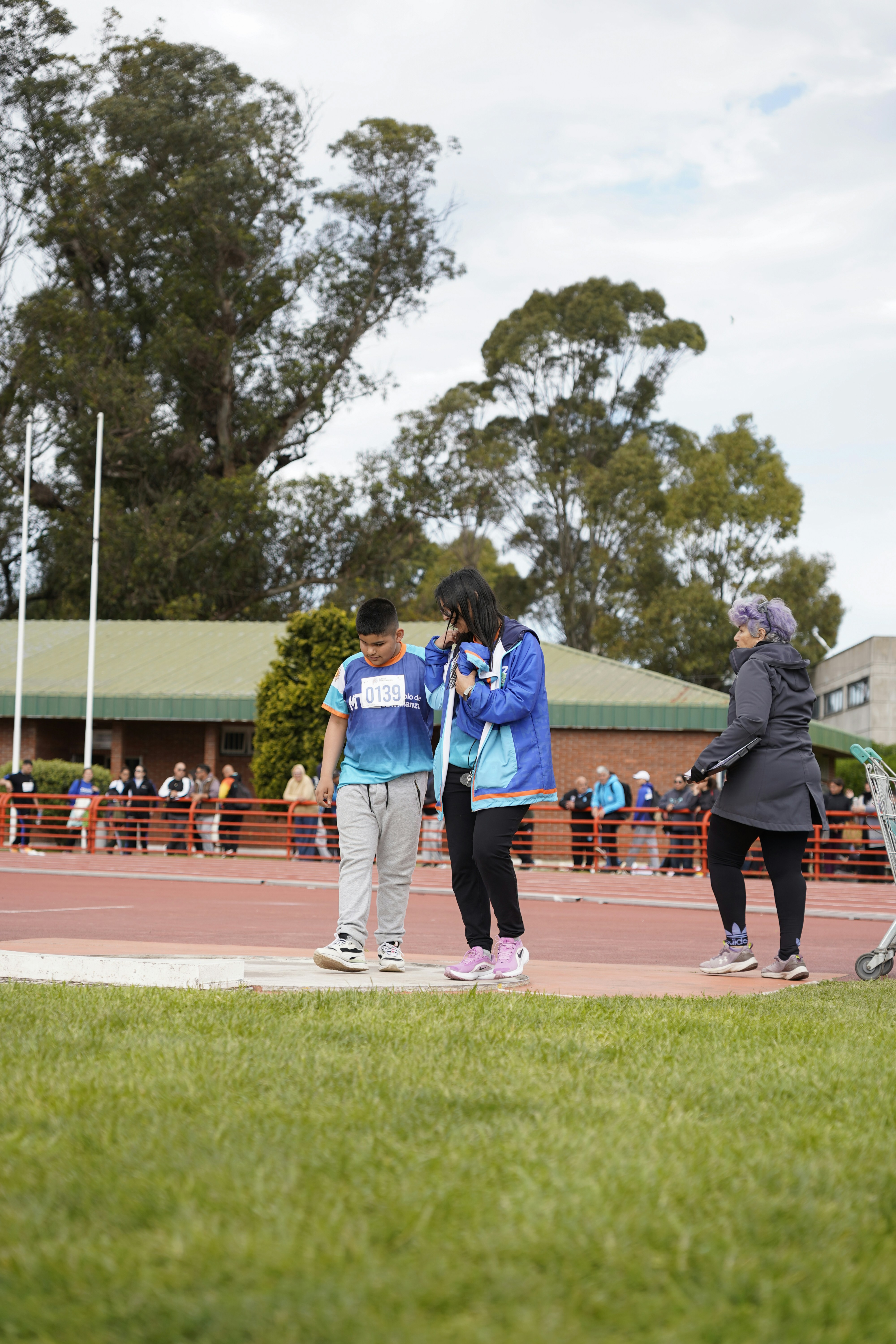 A person in a blue sports jersey and an adult walking on a red athletic track