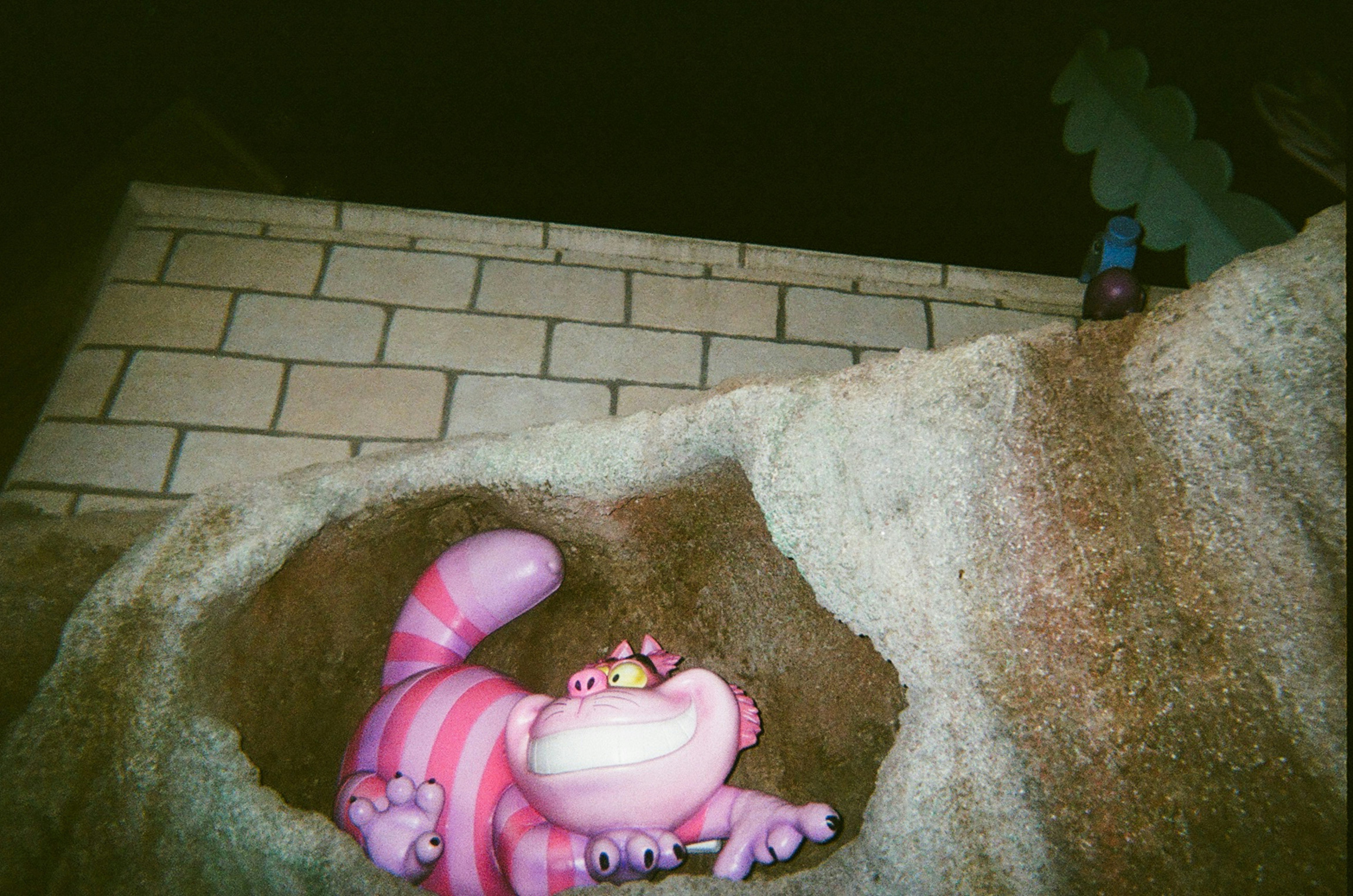 The Cheshire Cat figurine with pink stripes lying in a rocky cave entrance