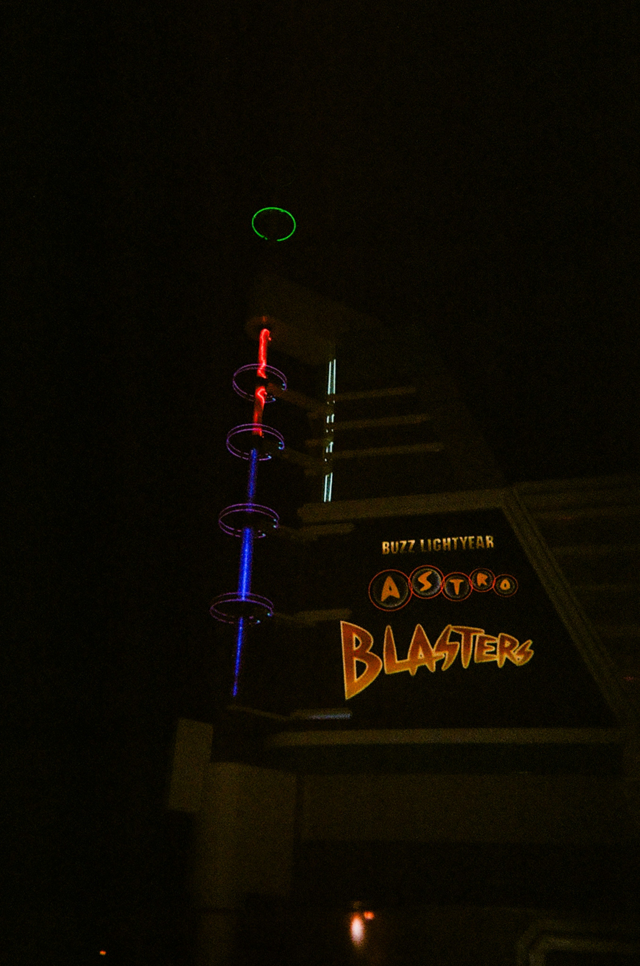 A neon sign reading Buzz Lightyear Astro Blasters with a glowing vertical light tower at night