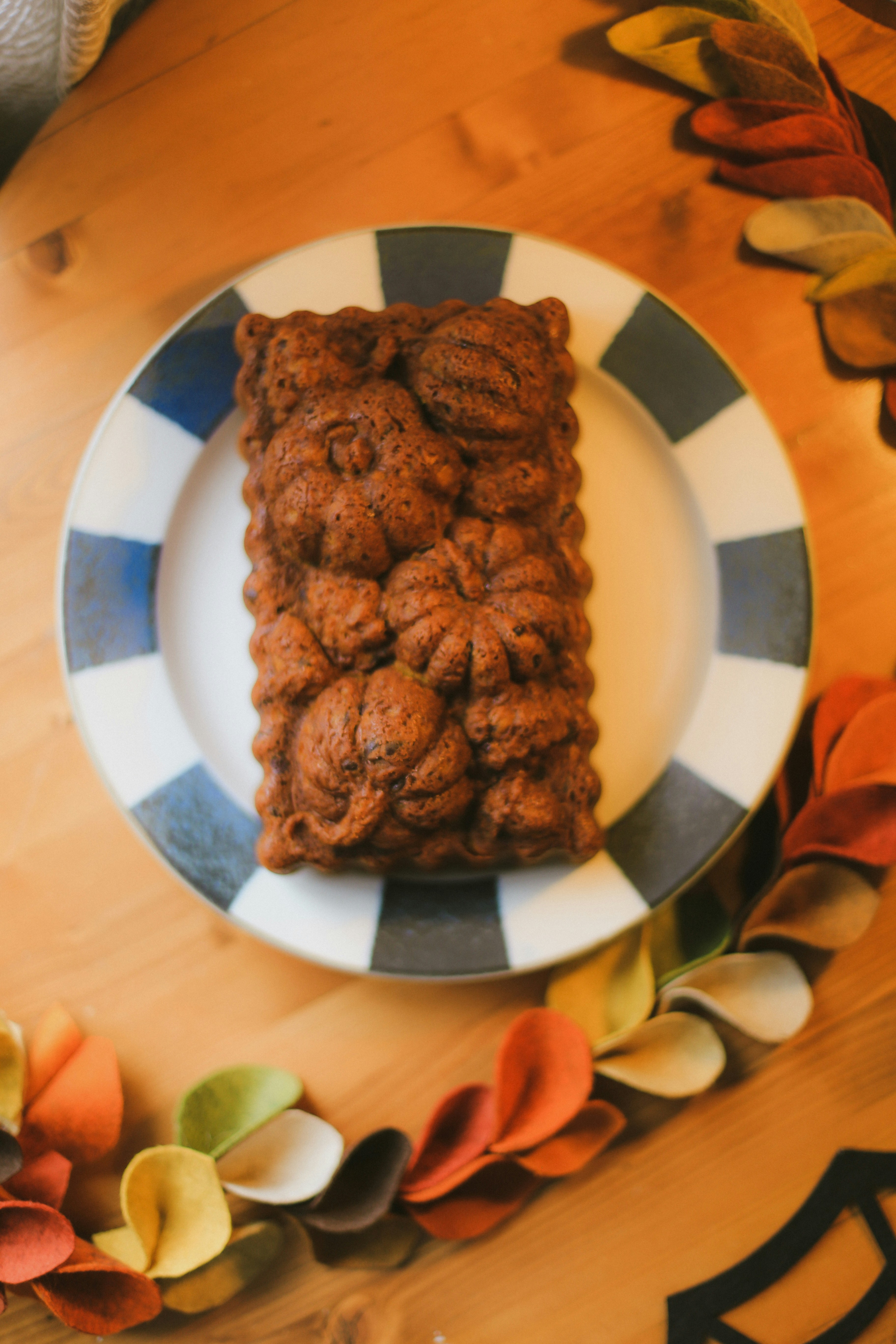 Loaf of pumpkin bread baked in a pumpkin-shaped pan on a plate with autumn leaves around it