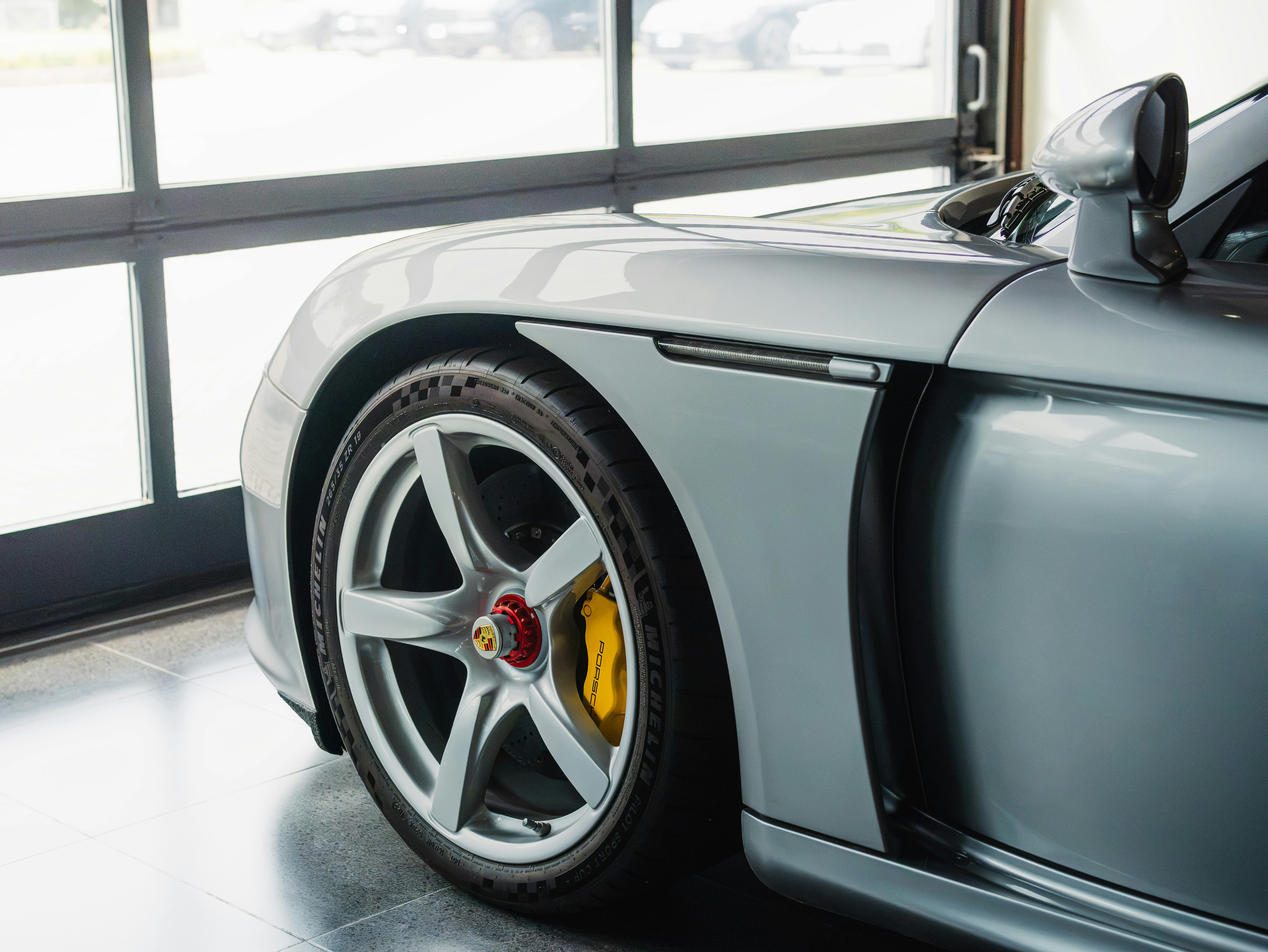 A silver Porsche Carrera GT parked in a garage with yellow brake calipers
