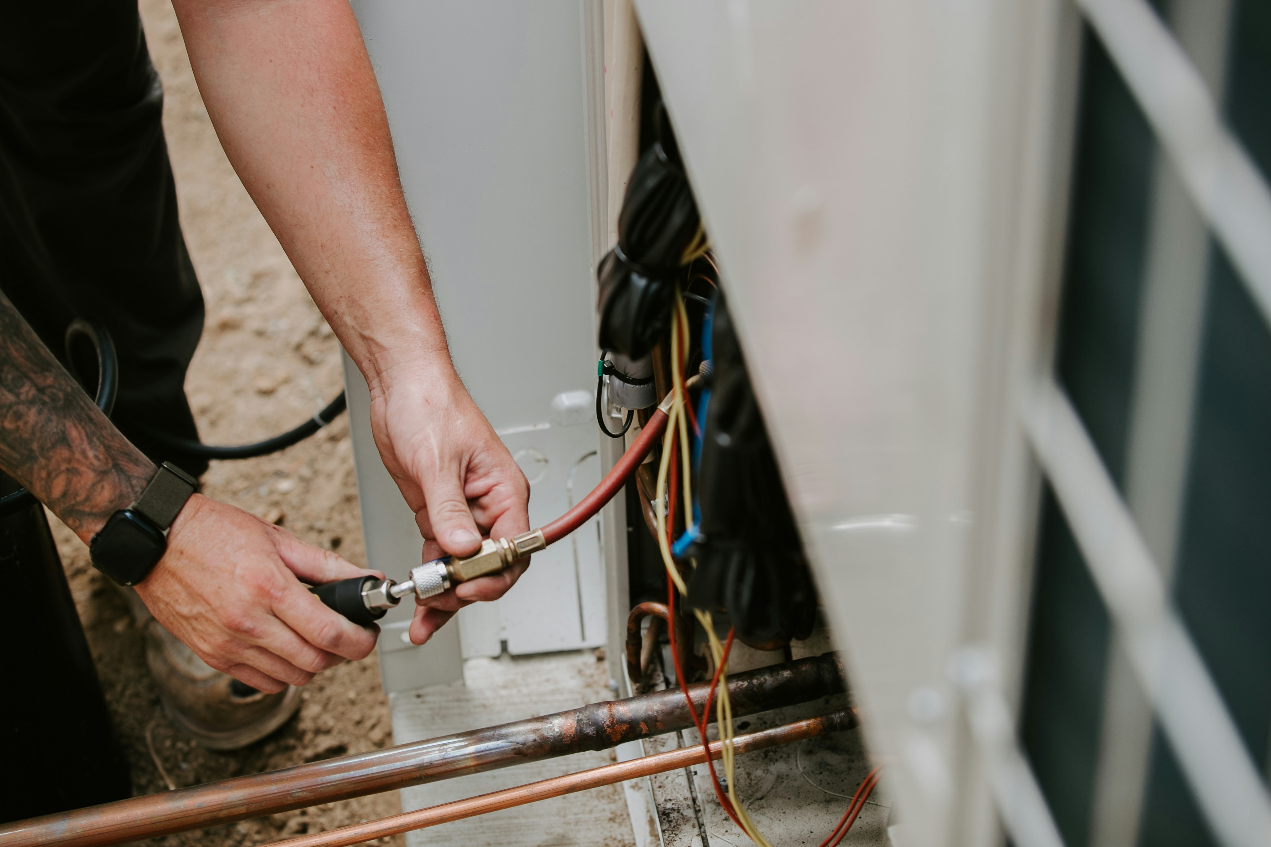 A technician connecting a hose to an outdoor air conditioning unit for maintenance