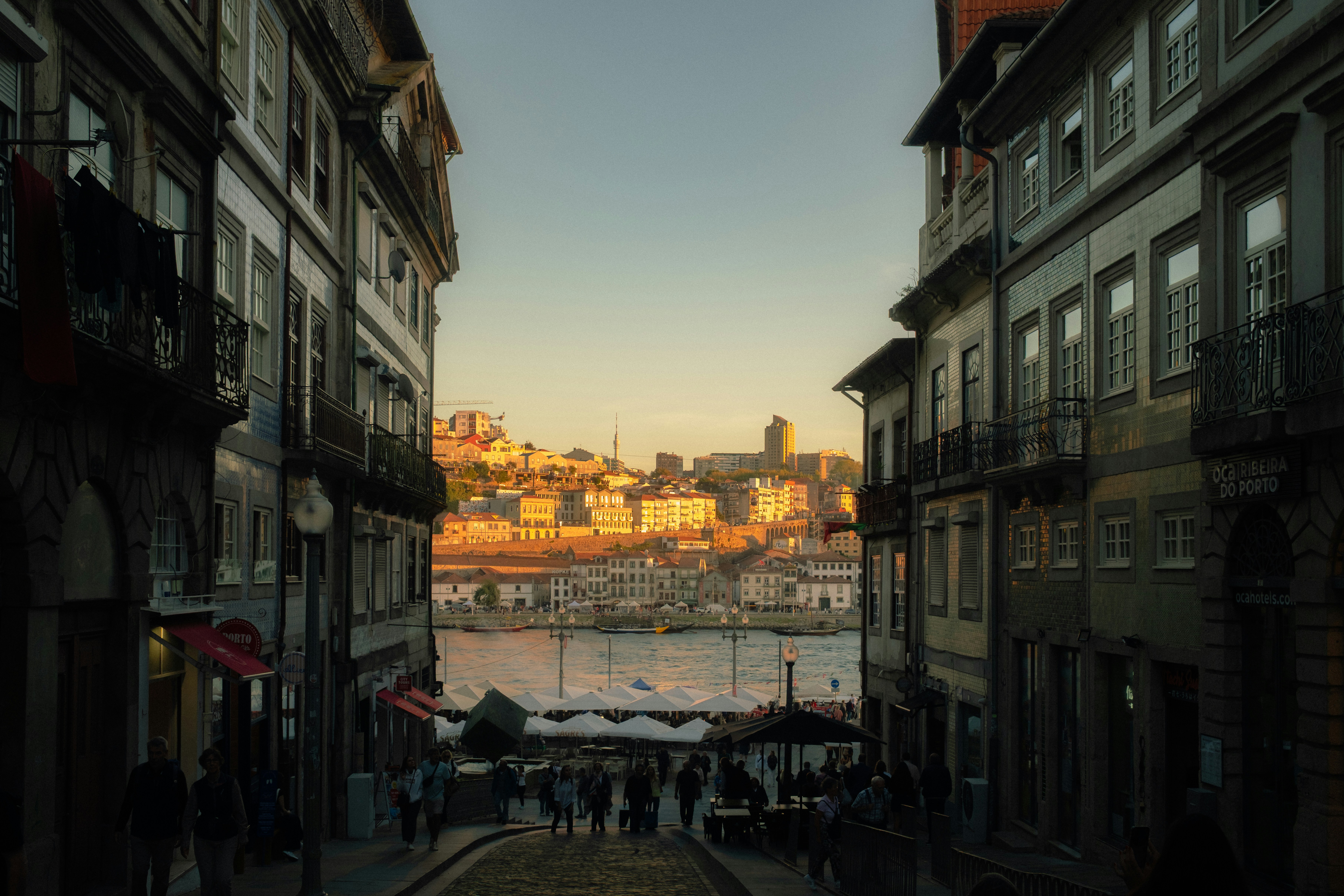 A narrow street leading to the Douro River in Porto with historic buildings and golden light
