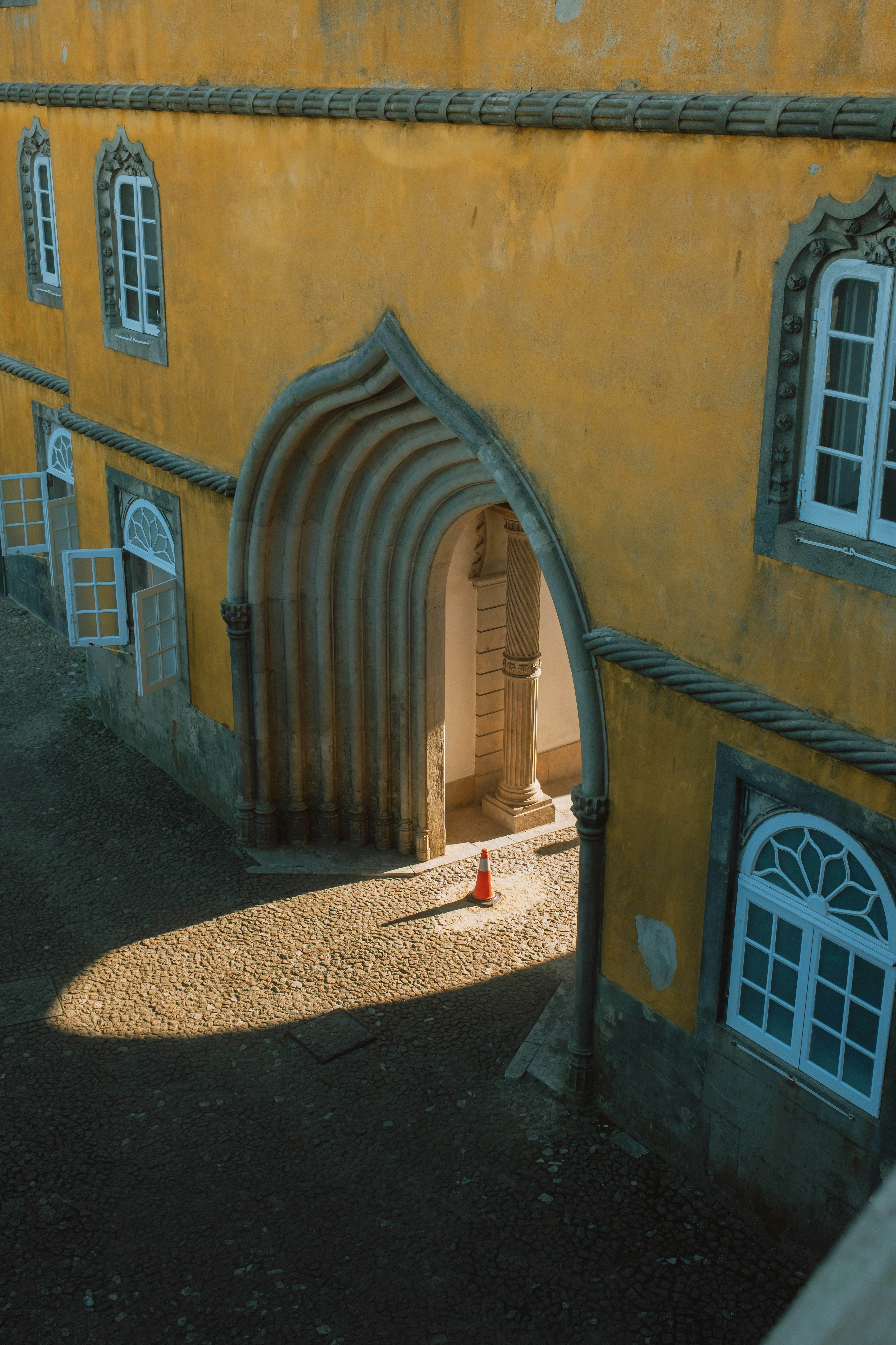 A single orange traffic cone on a cobblestone courtyard beneath a yellow arched building entrance - 相关推荐