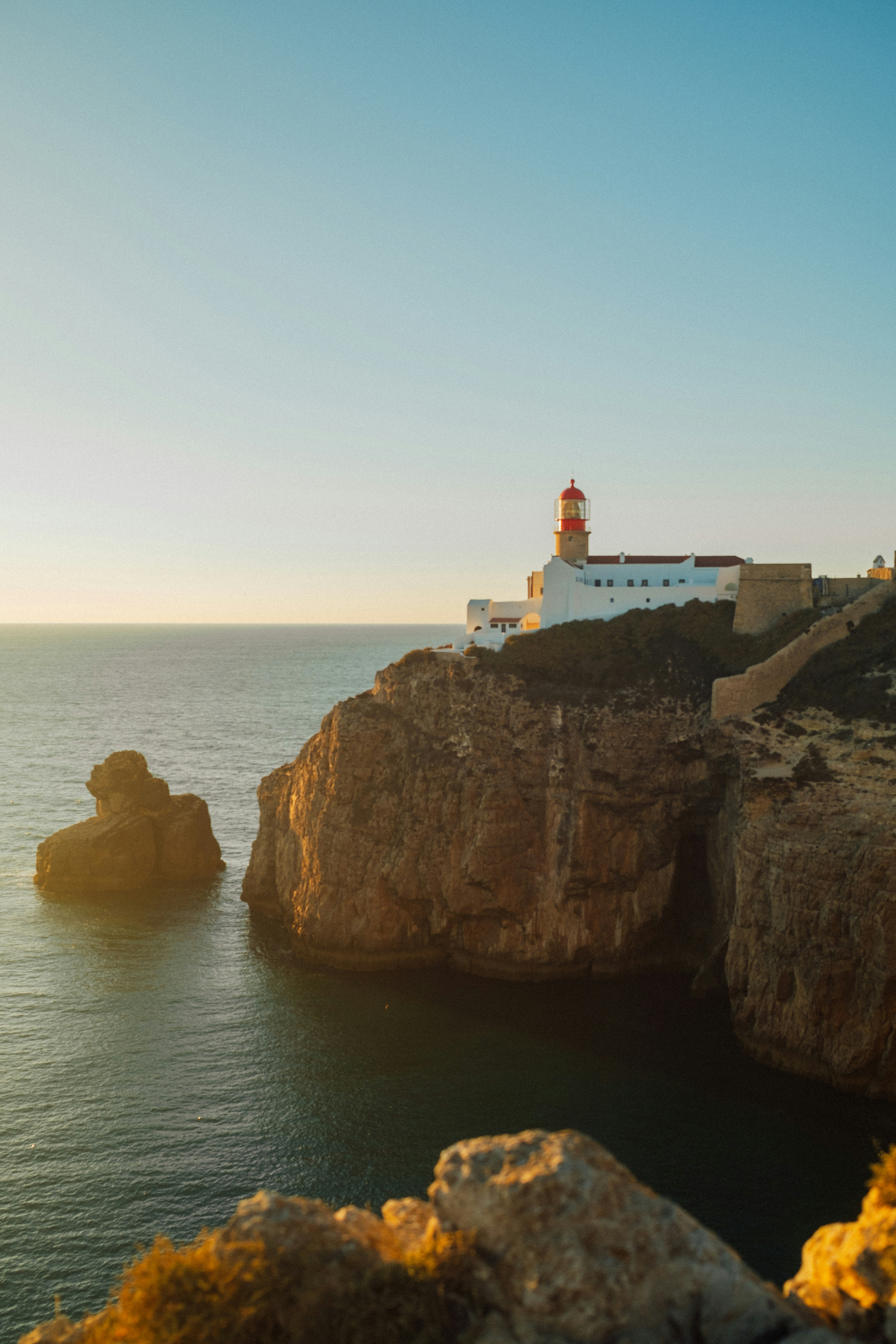 A lighthouse with a red top on a rocky cliff above the ocean at golden hour - 相关推荐