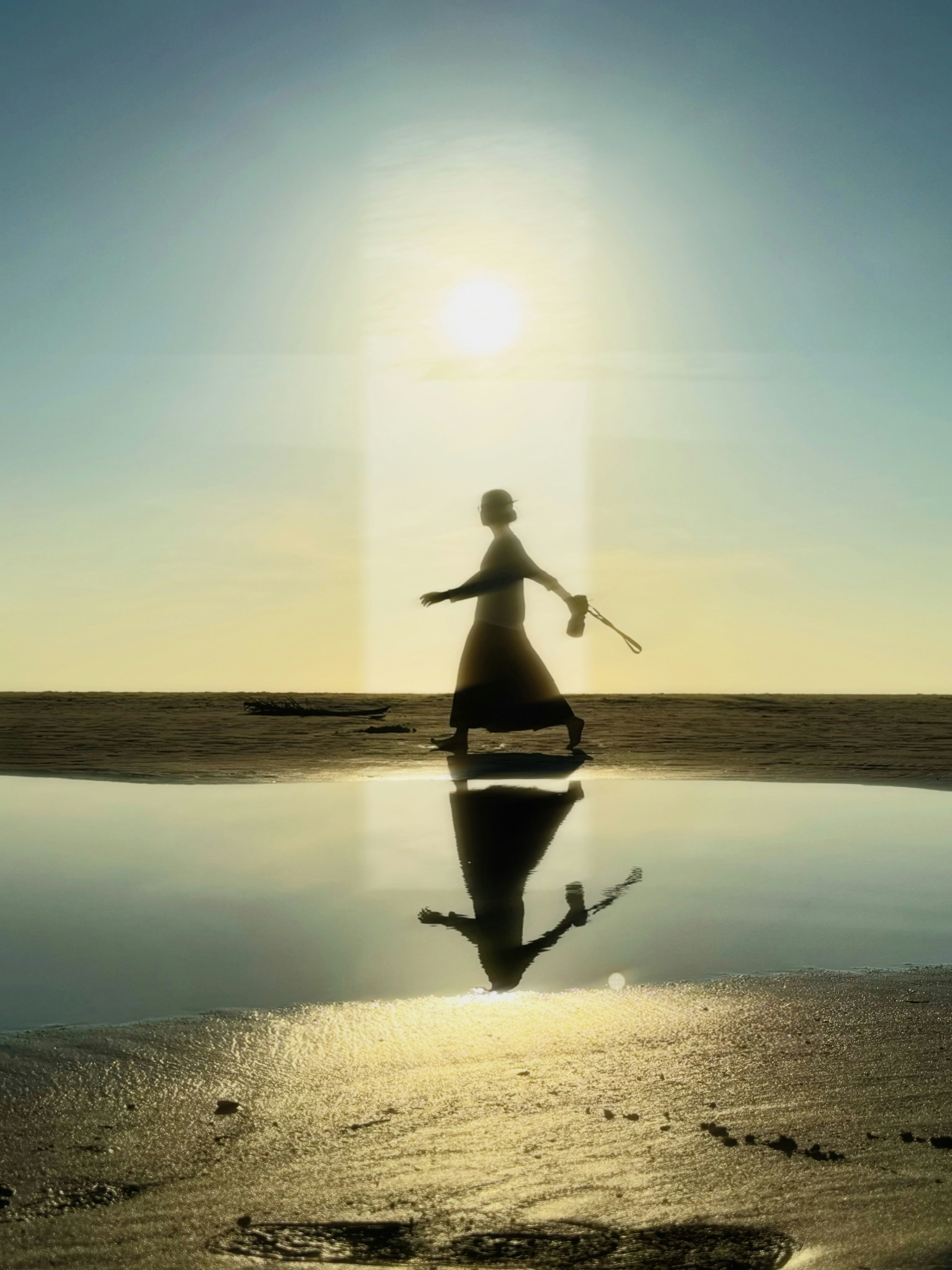 A person in silhouette walking on a beach with a reflection in a tidal pool - 相关推荐