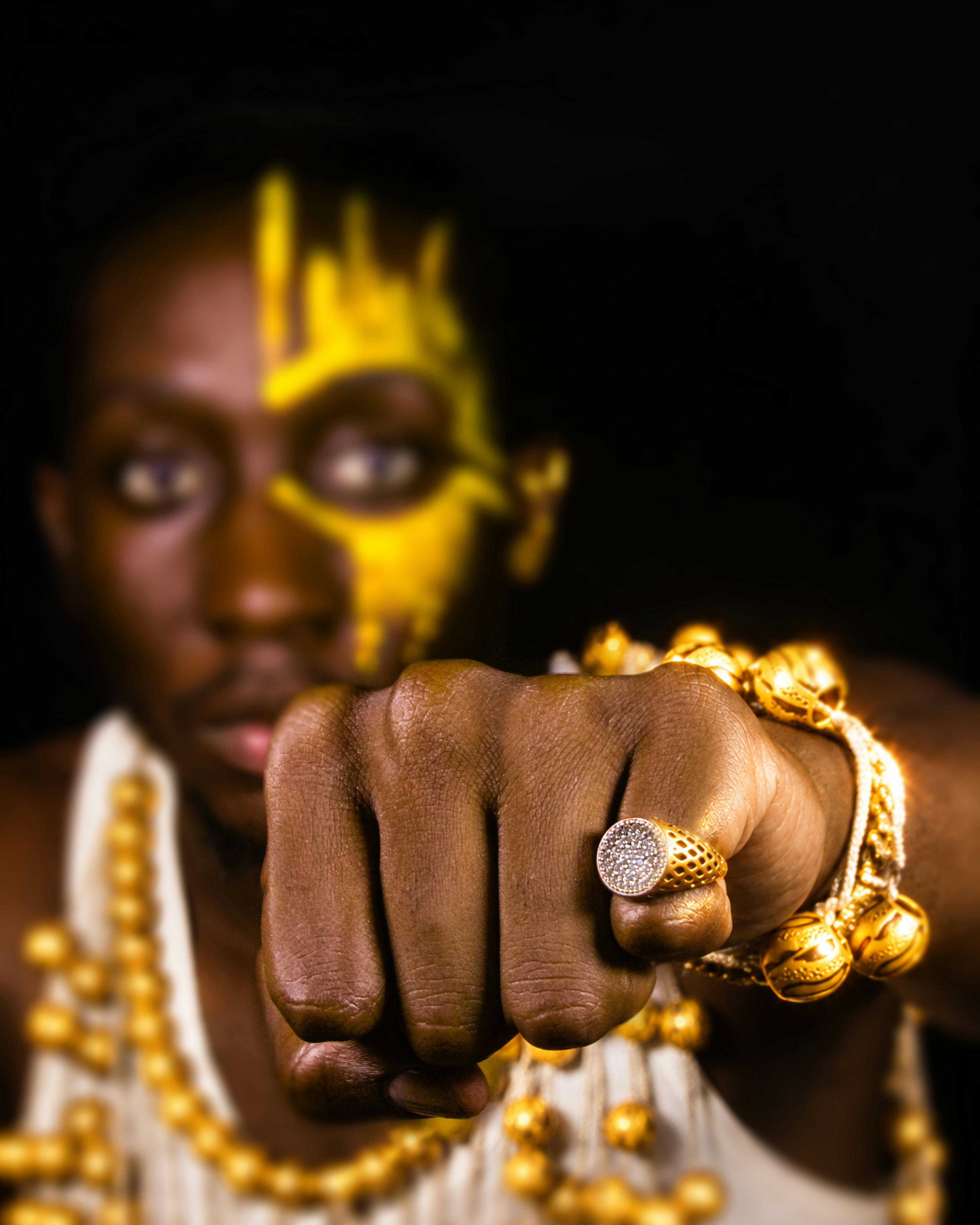 A person with yellow face paint and gold jewelry extending a fist toward the camera