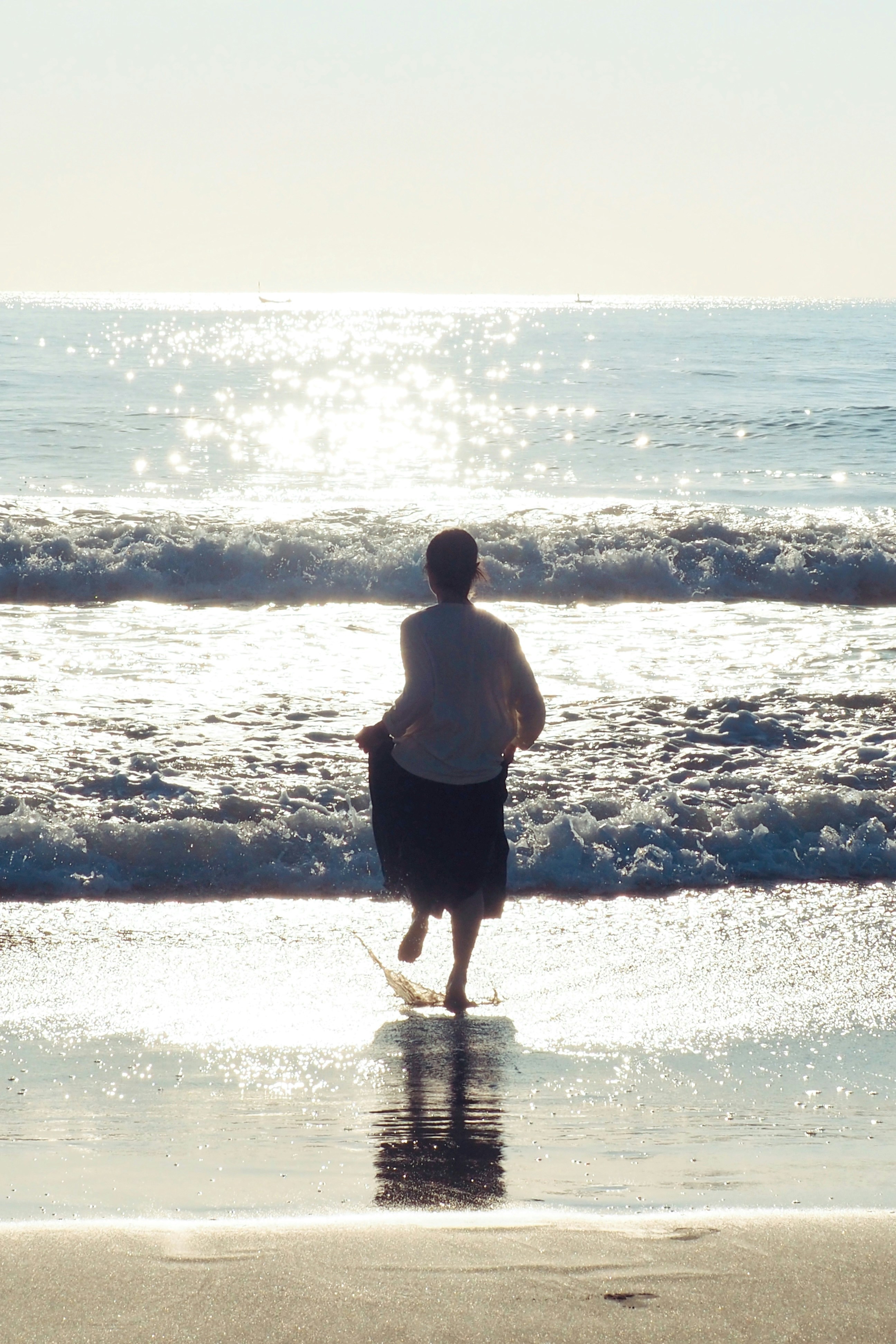 A person in a light shirt and dark skirt running into the ocean surf - 相关推荐