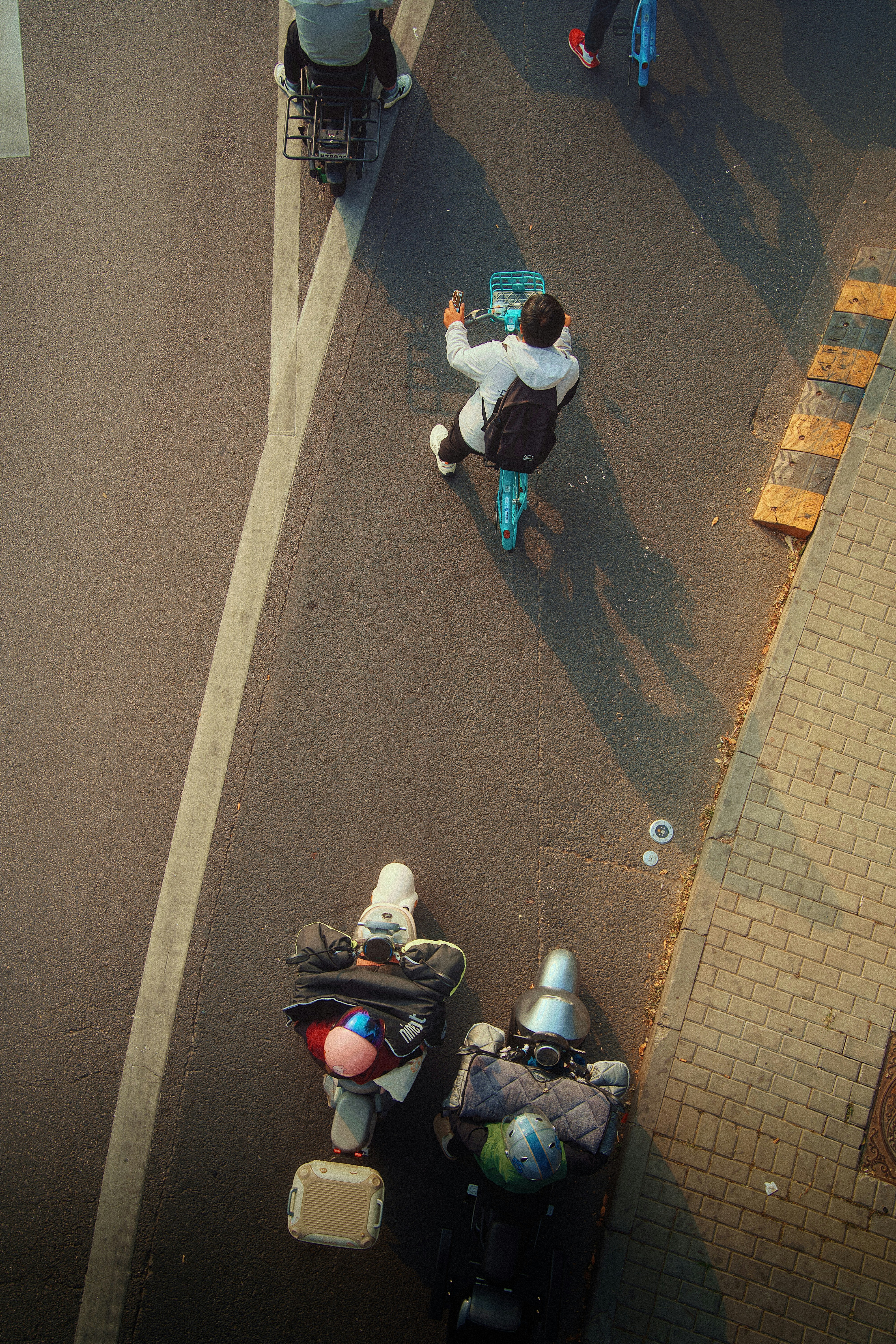 An aerial view of people on bicycles and scooters on a paved road in warm light - 相关推荐