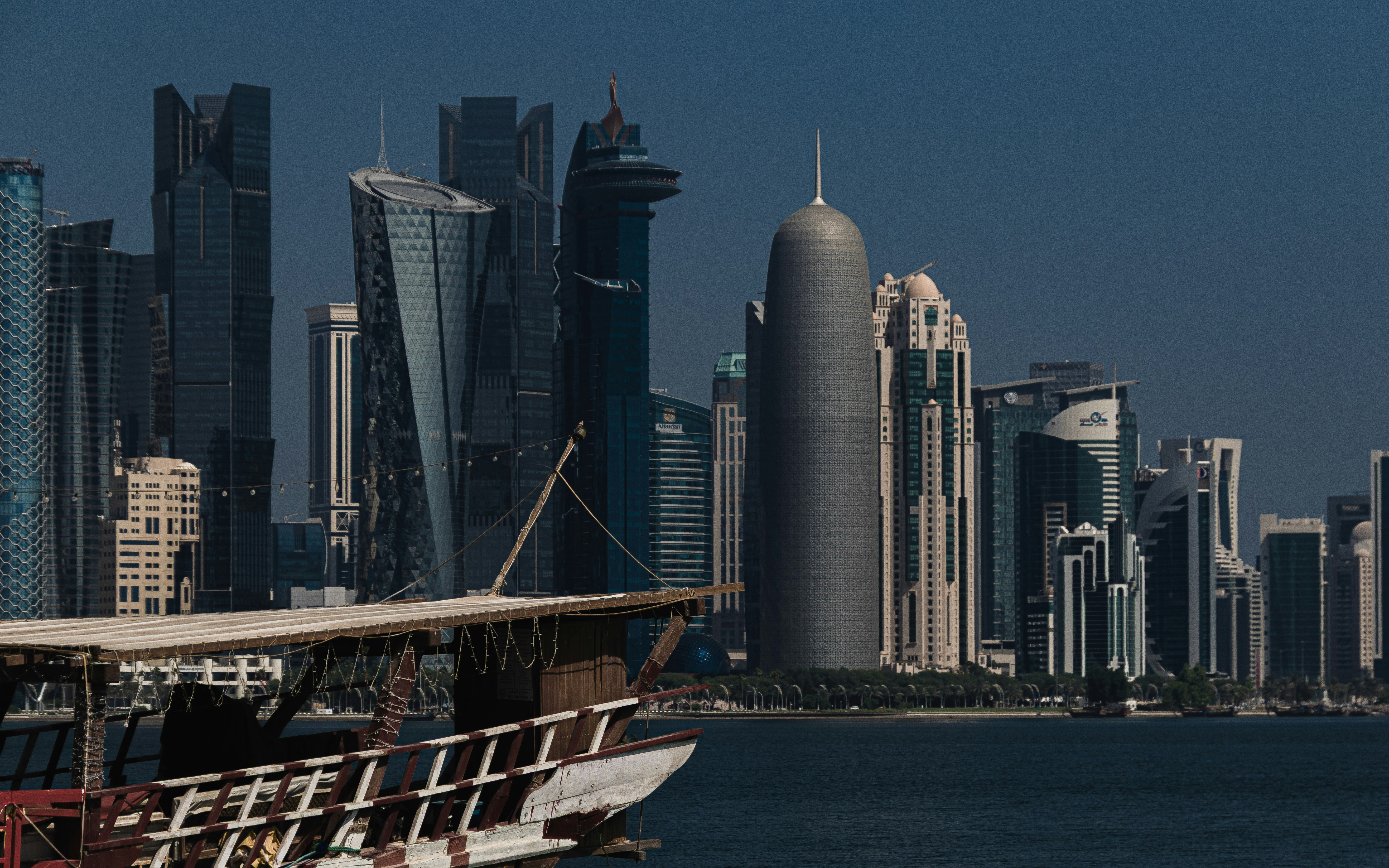 A traditional wooden dhow boat in the foreground against the modern skyline of Doha, Qatar
