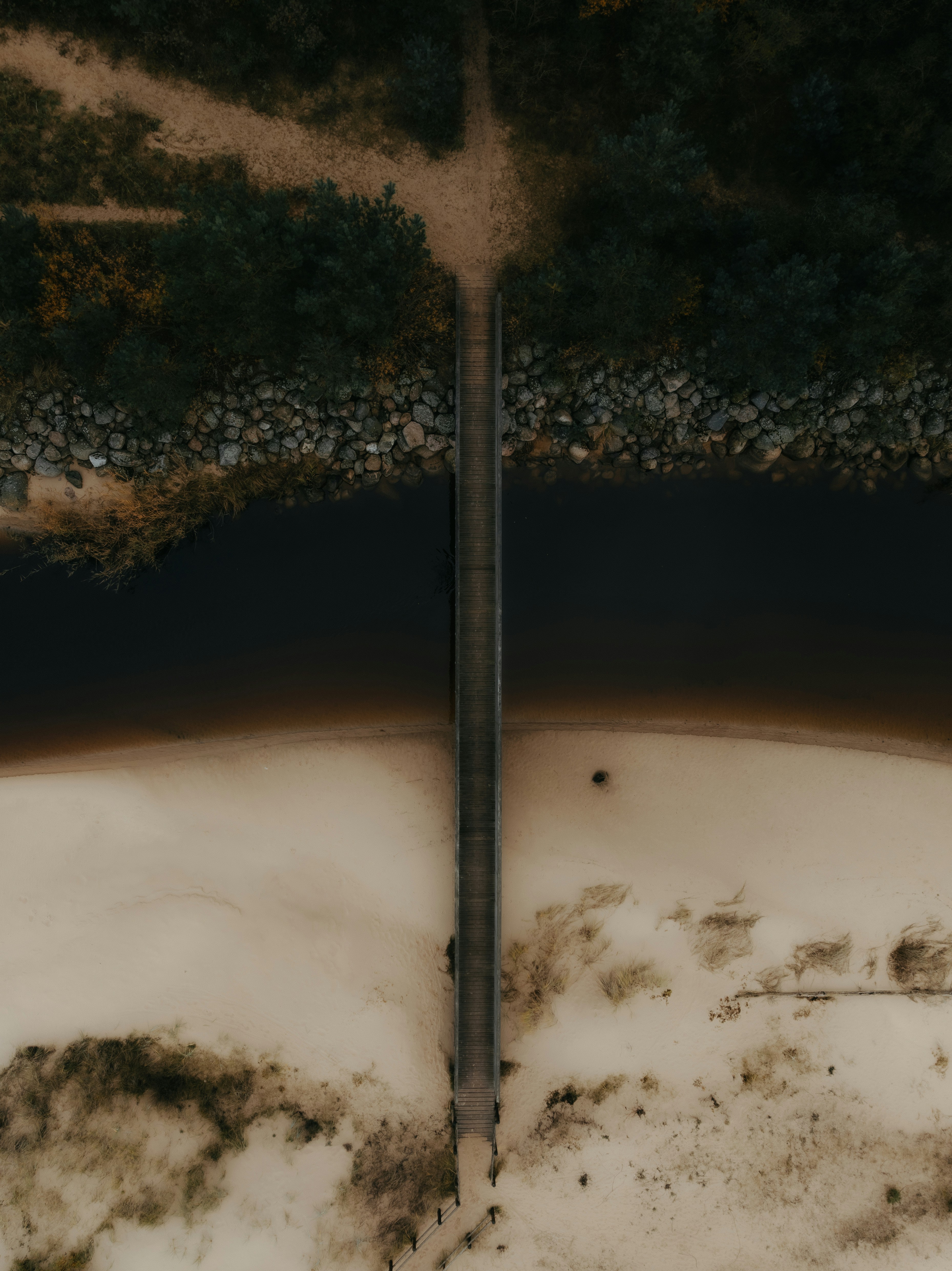 An aerial view of a wooden footbridge crossing a dark river to a sandy beach - 相关推荐