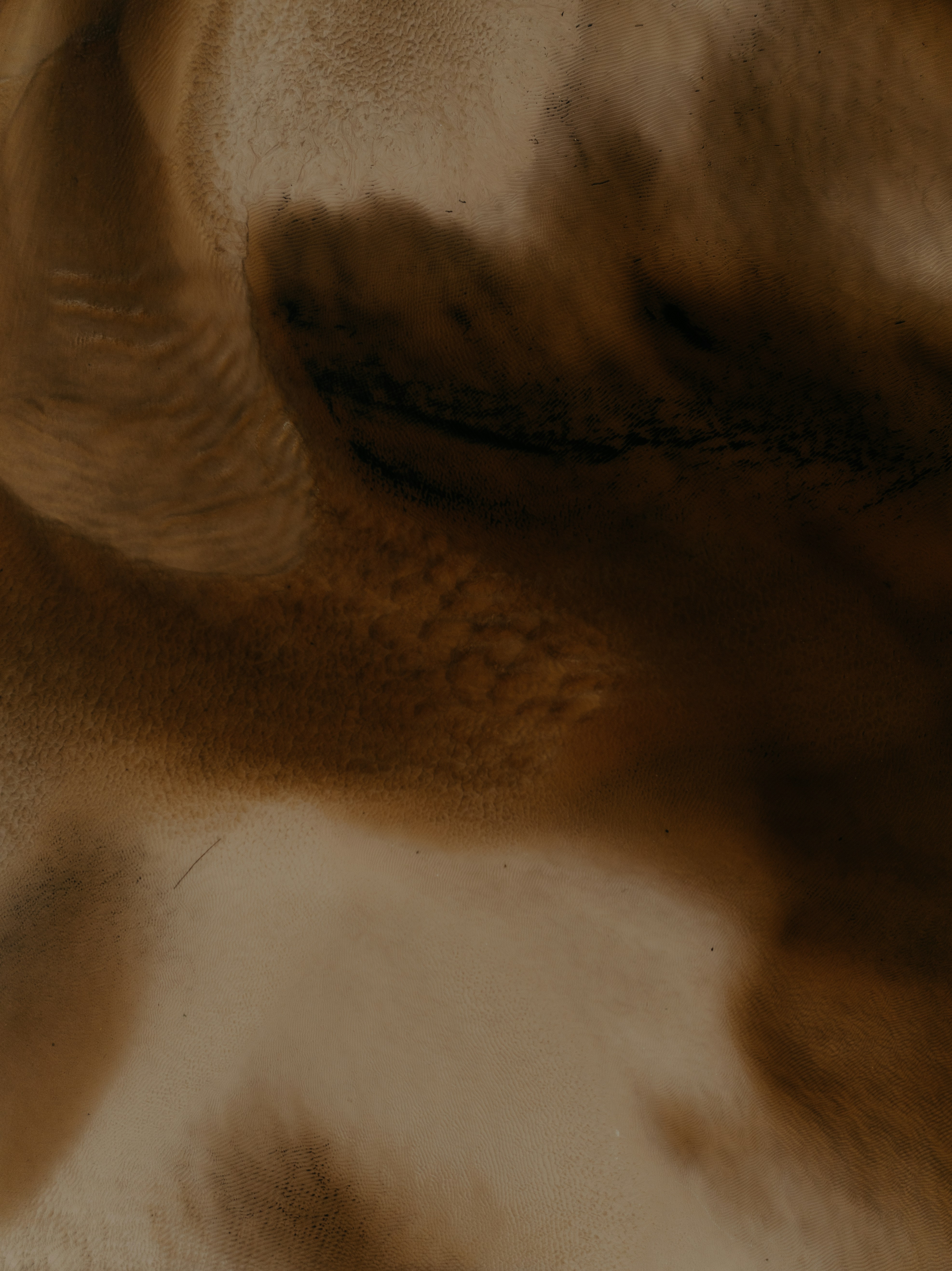 An aerial view of rippled brown sand dunes and dark shadows - 相关推荐