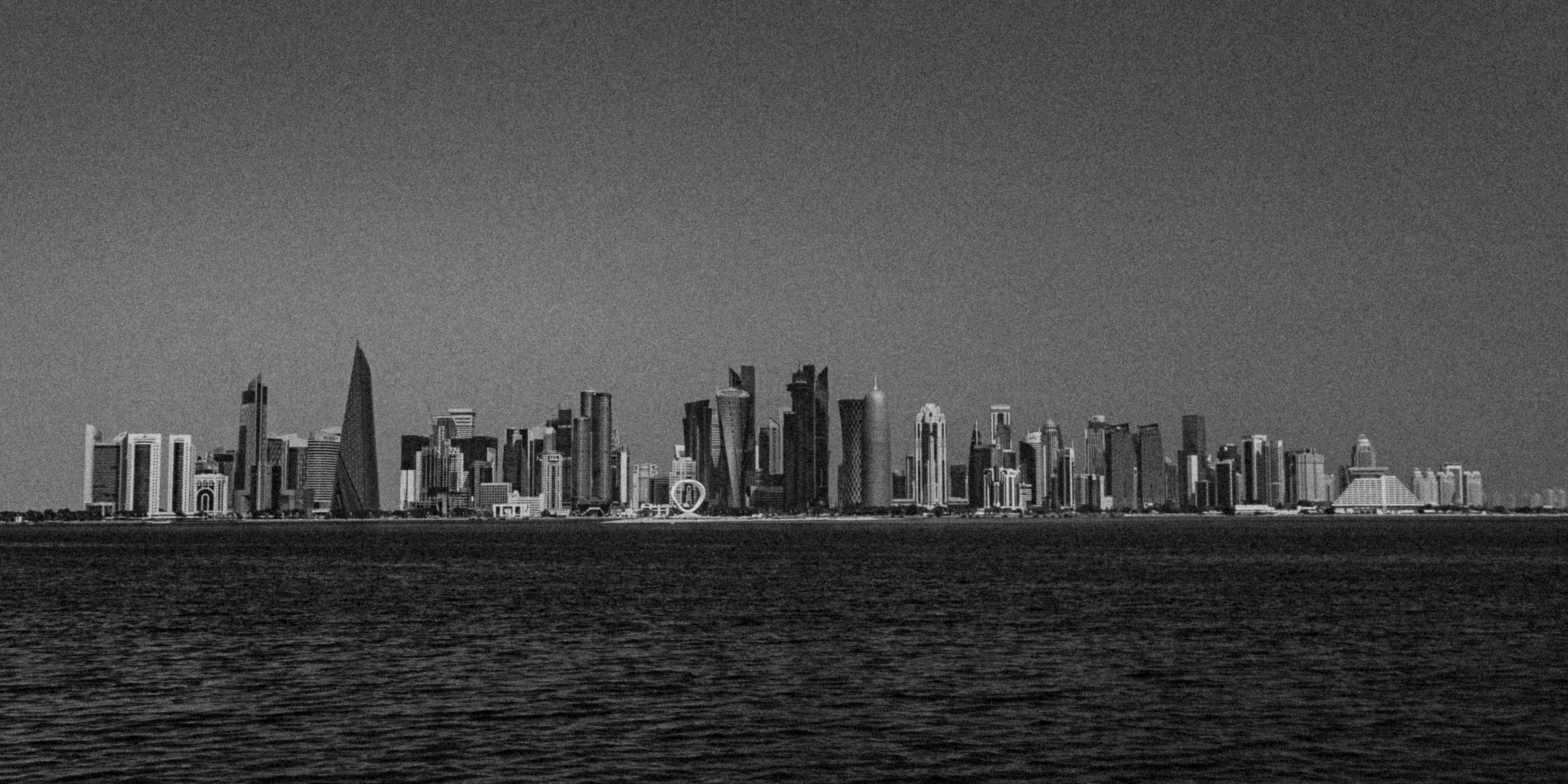 A black and white panoramic view of the Doha skyline across the calm water