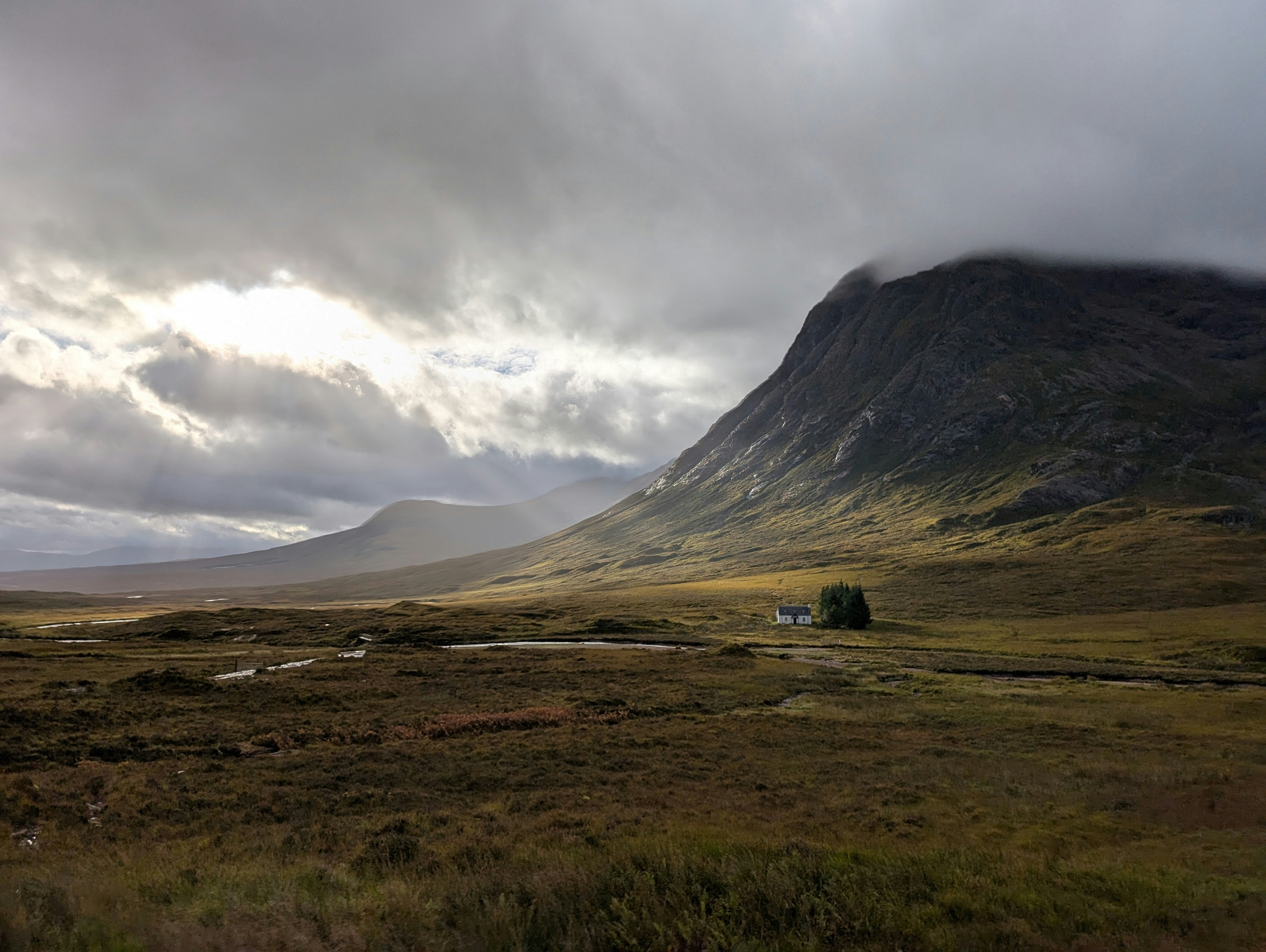 A small white house in a vast valley beneath a large mountain under cloudy skies - 相关推荐