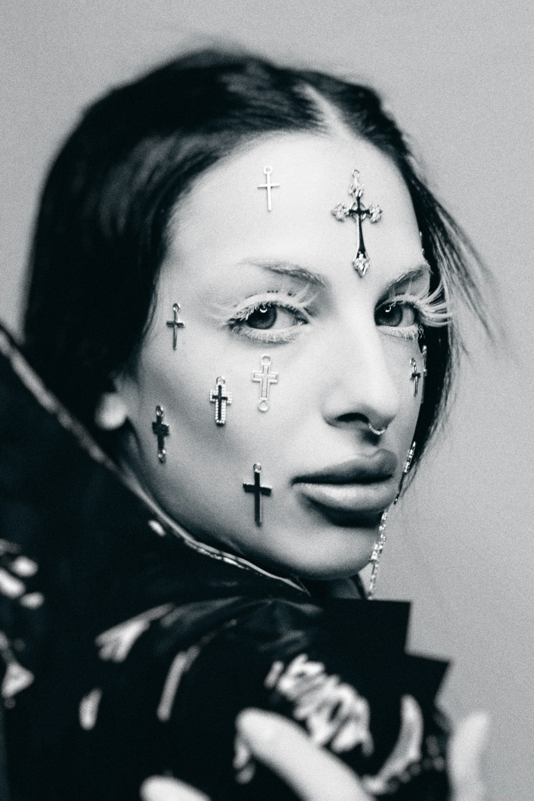 A person with small cross charms adhered to their face and long white eyelashes