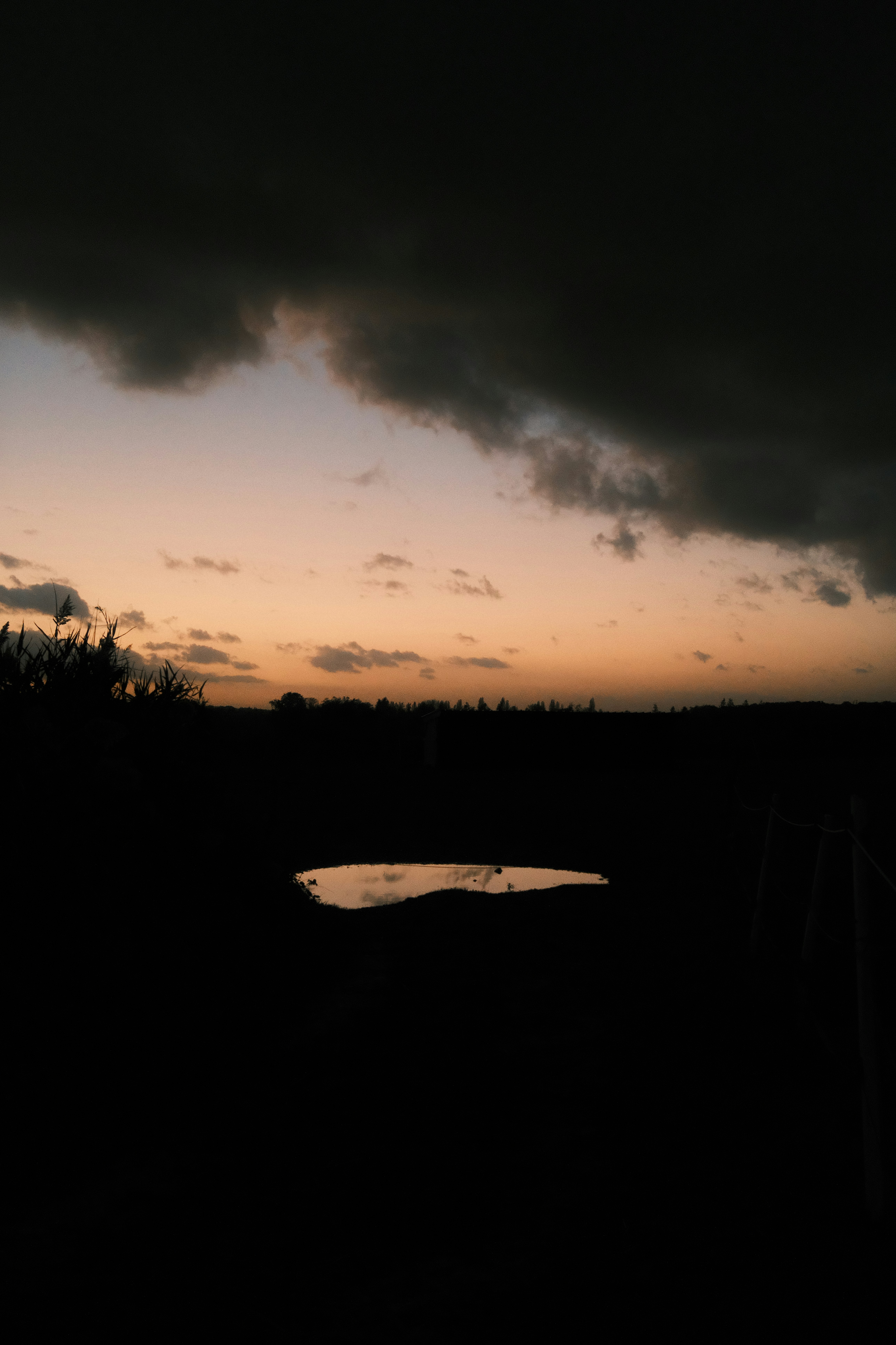 A small puddle reflecting a warm orange sky beneath dark storm clouds - 相关推荐