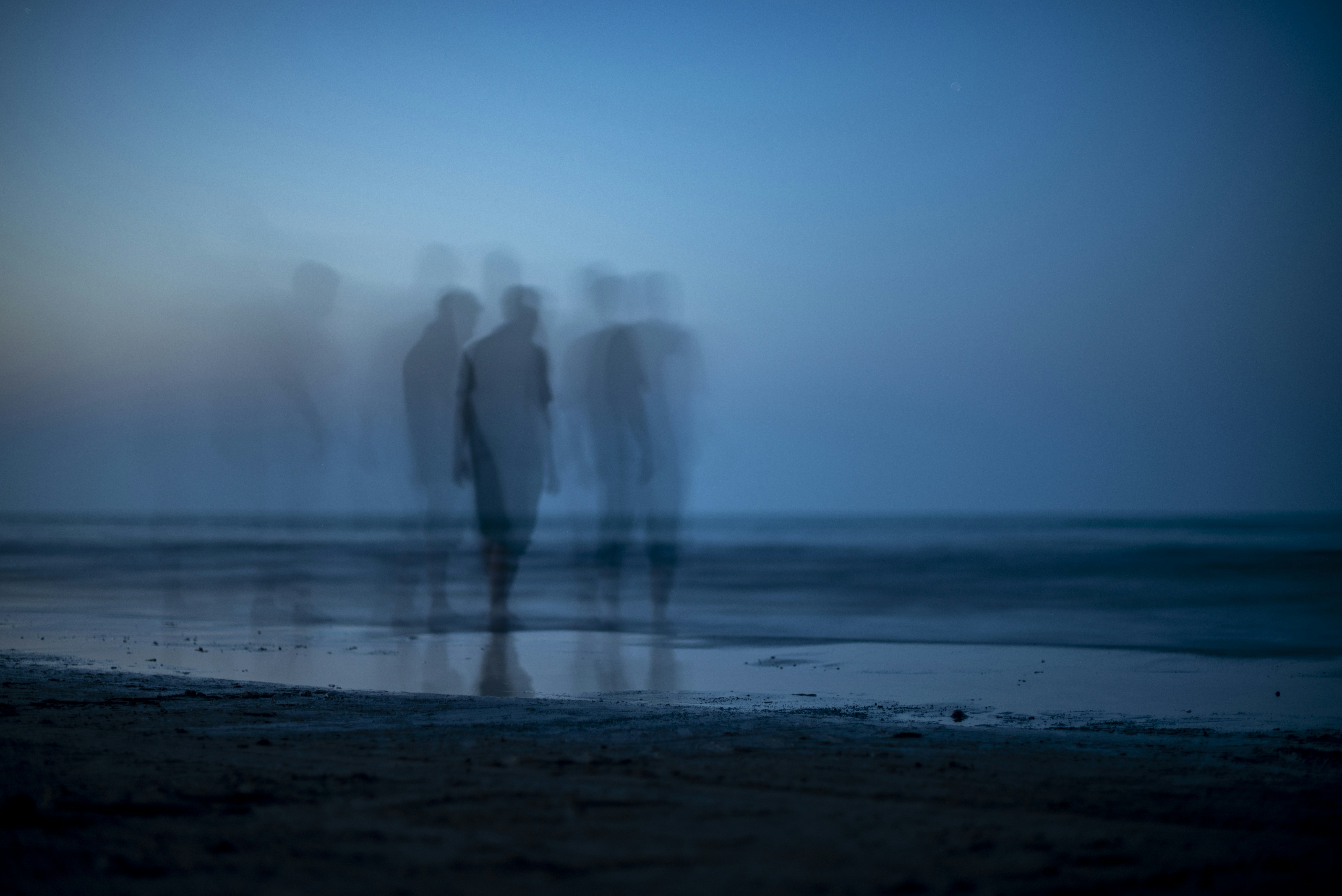 Blurred figures of people walking along a dark beach during the blue hour