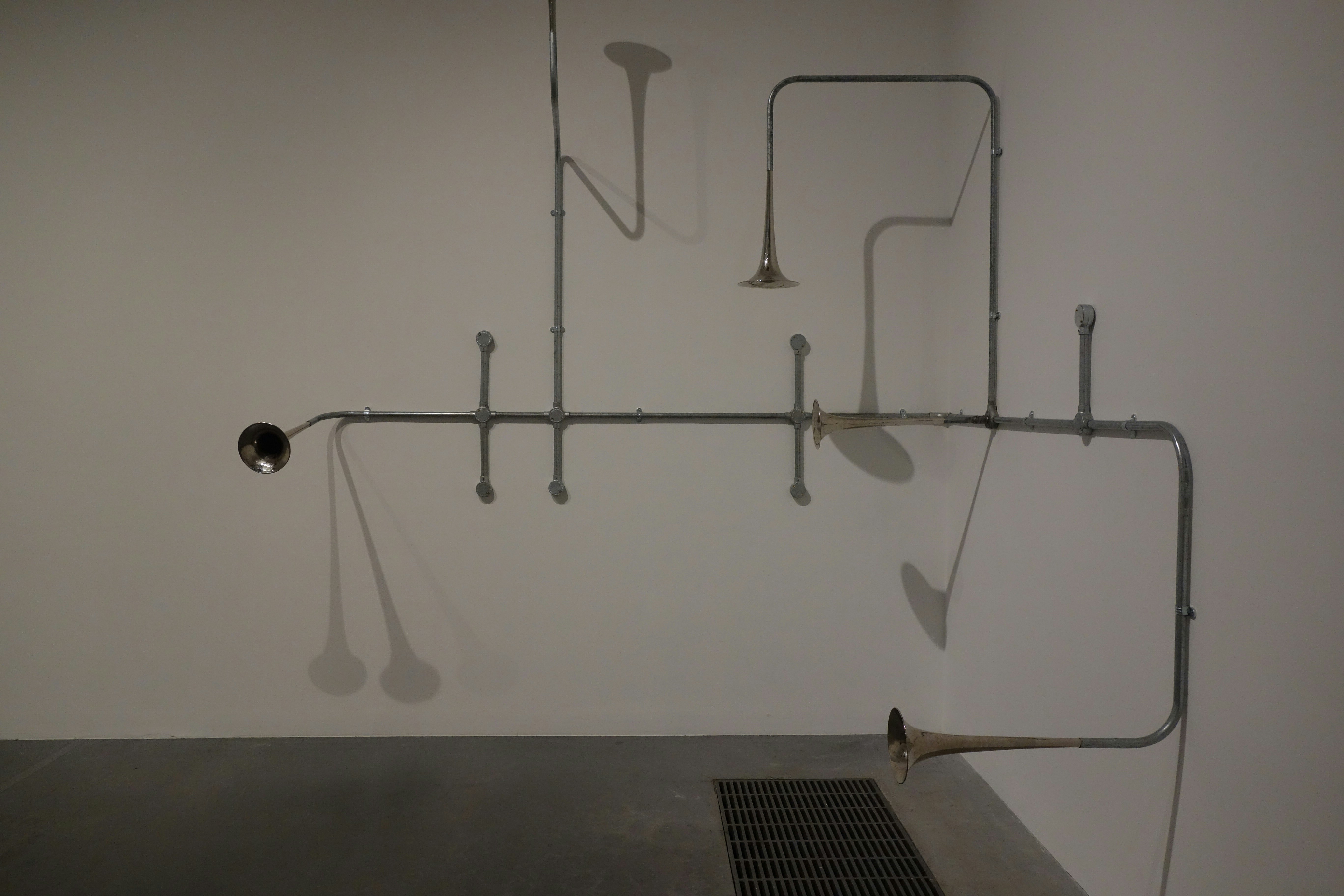 Metal pipes mounted on a white wall with trumpet-like bells extending into the room