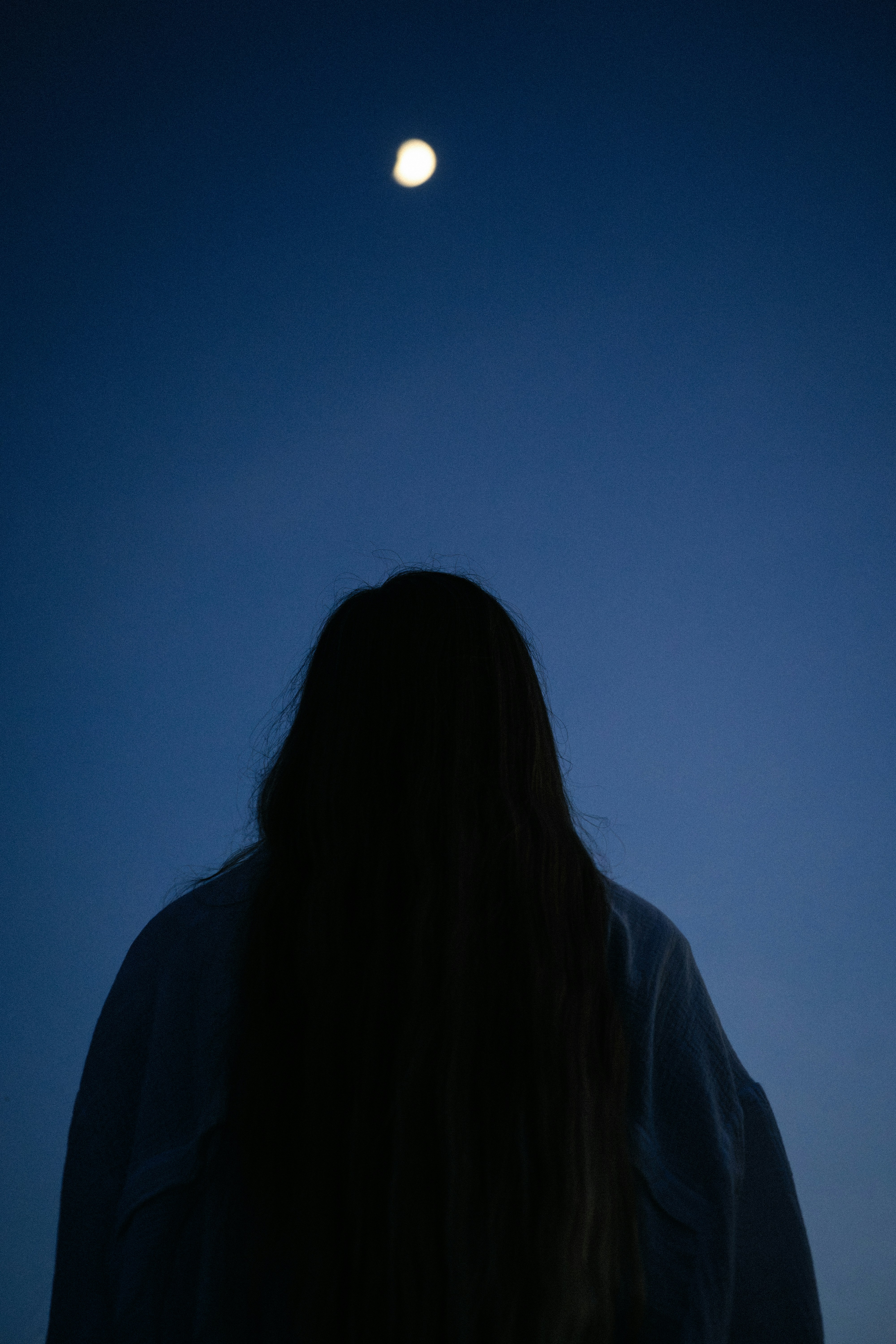 A person with long hair in silhouette against a deep blue evening sky with a bright moon - 相关推荐