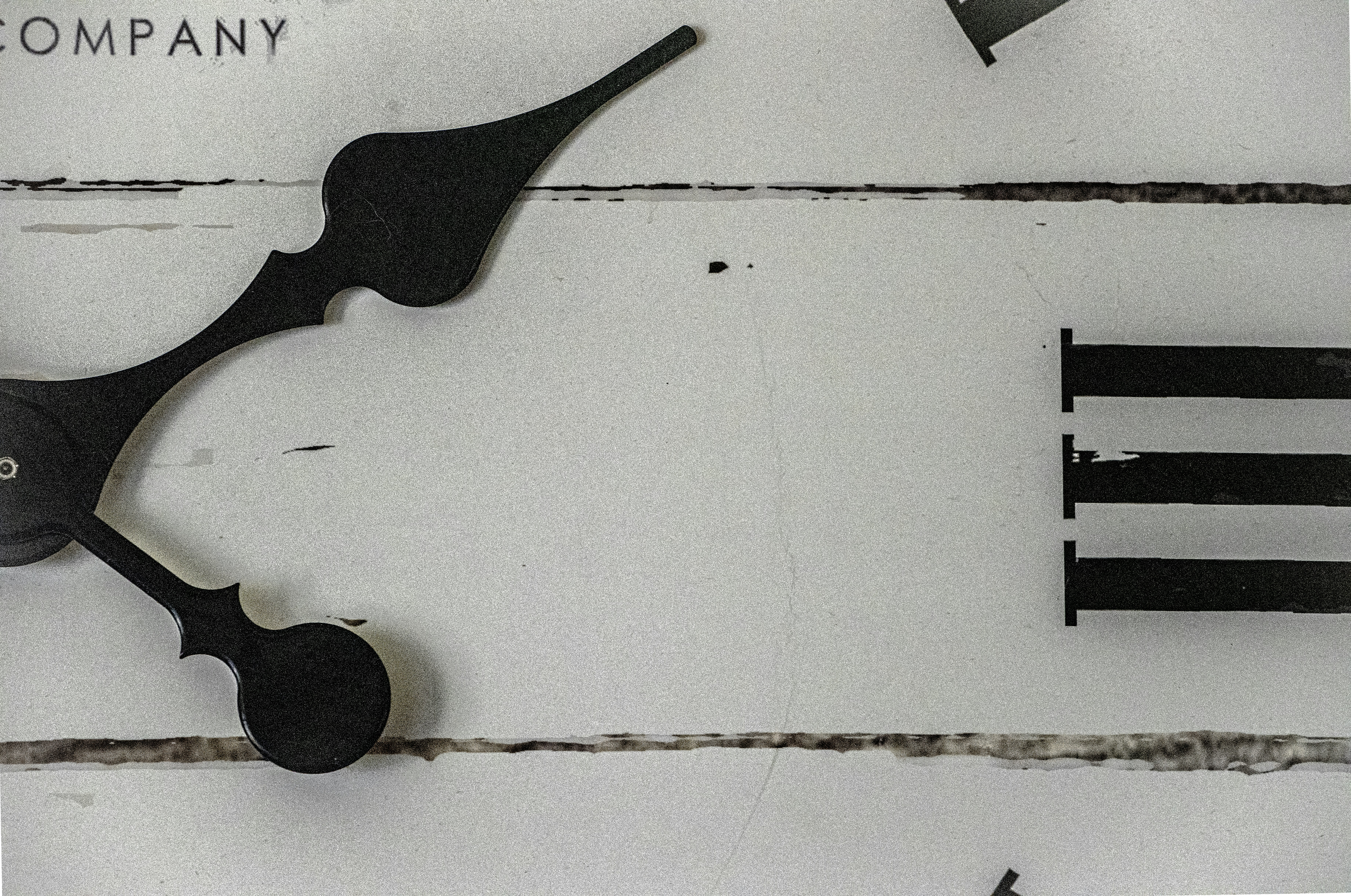 A close-up of black clock hands on a distressed white wooden clock face