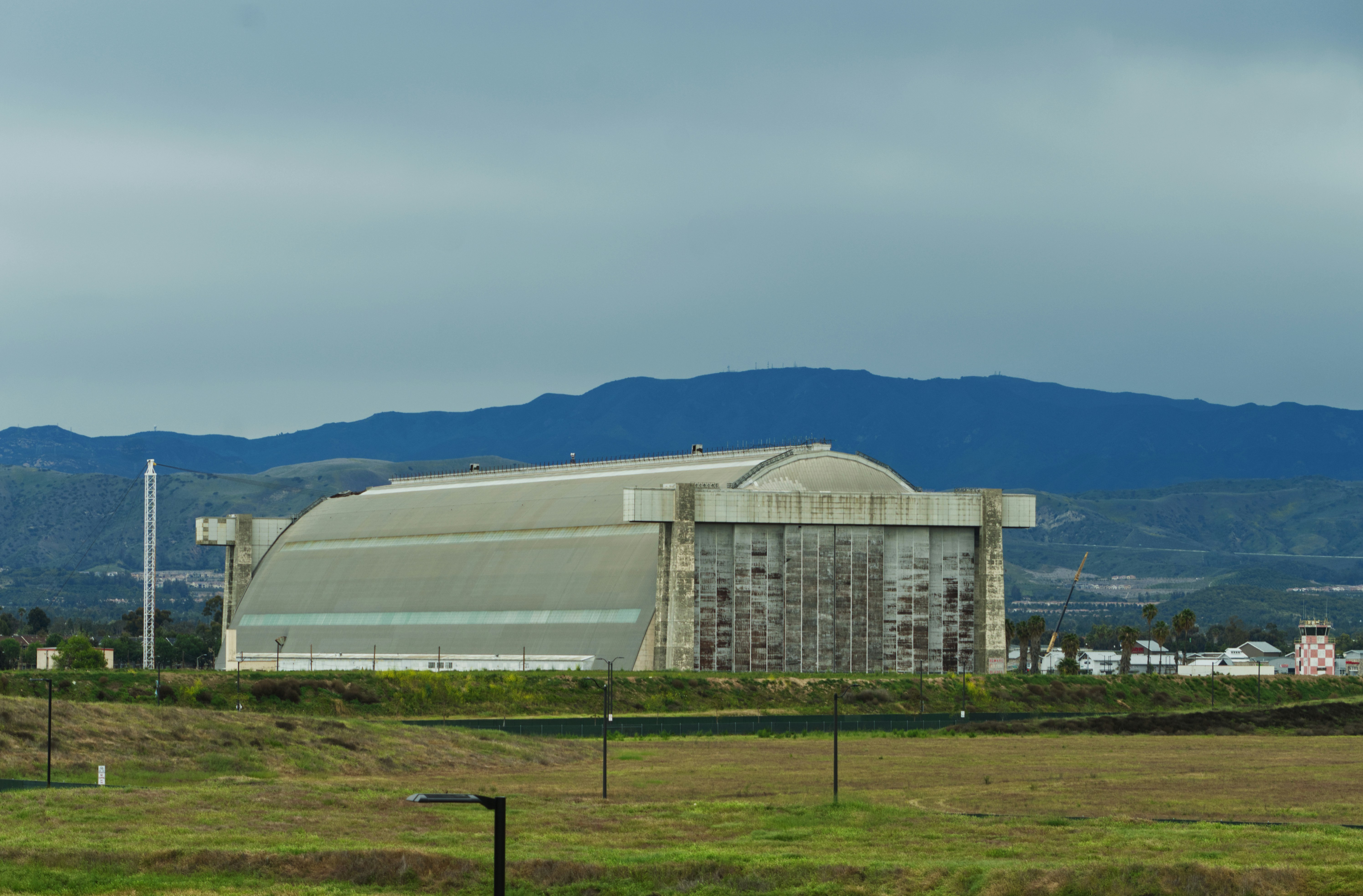 A large arched hangar building in a field with mountains in the distance