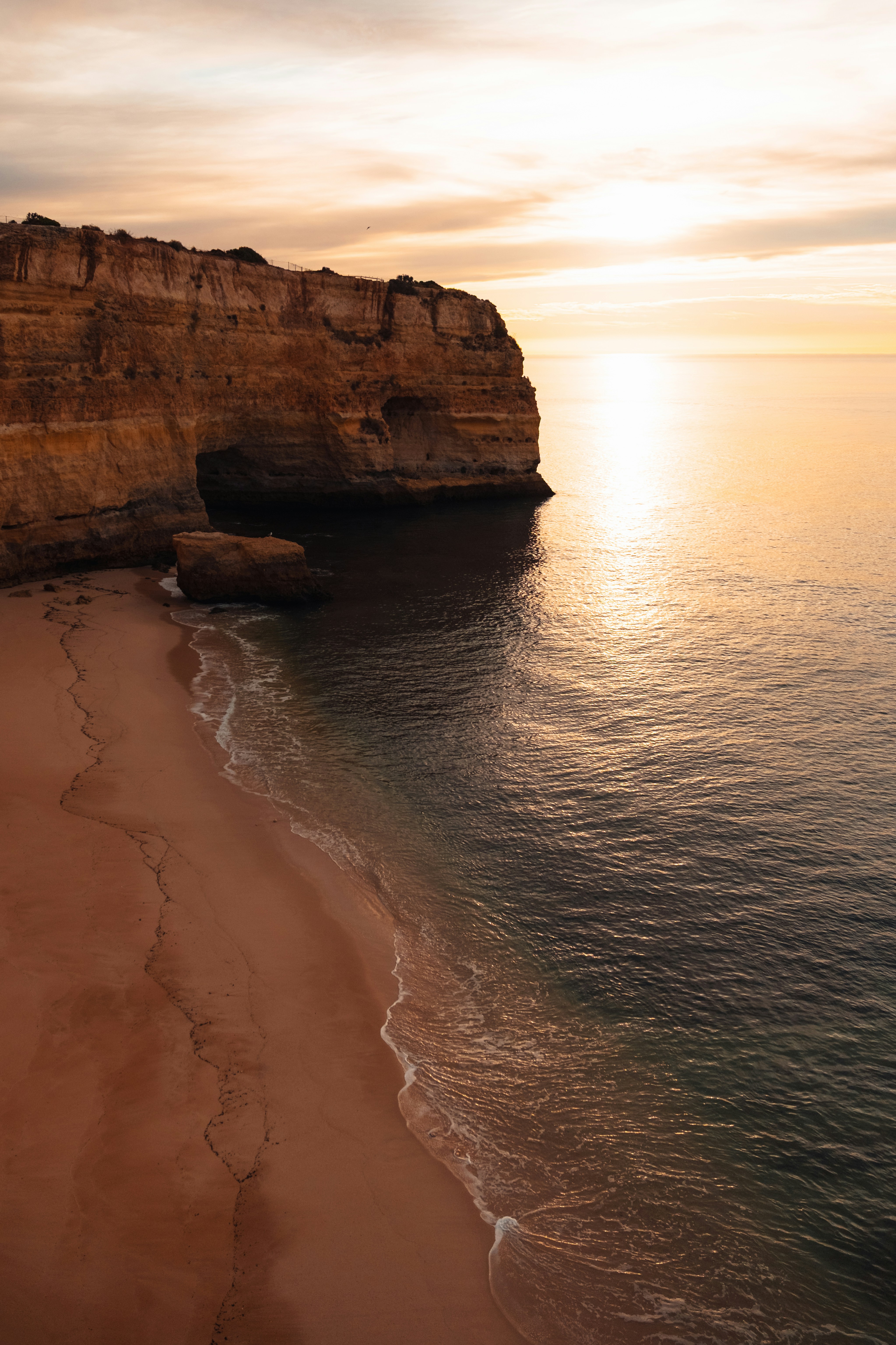 A sandy beach below tall golden cliffs at low sun with calm ocean water
