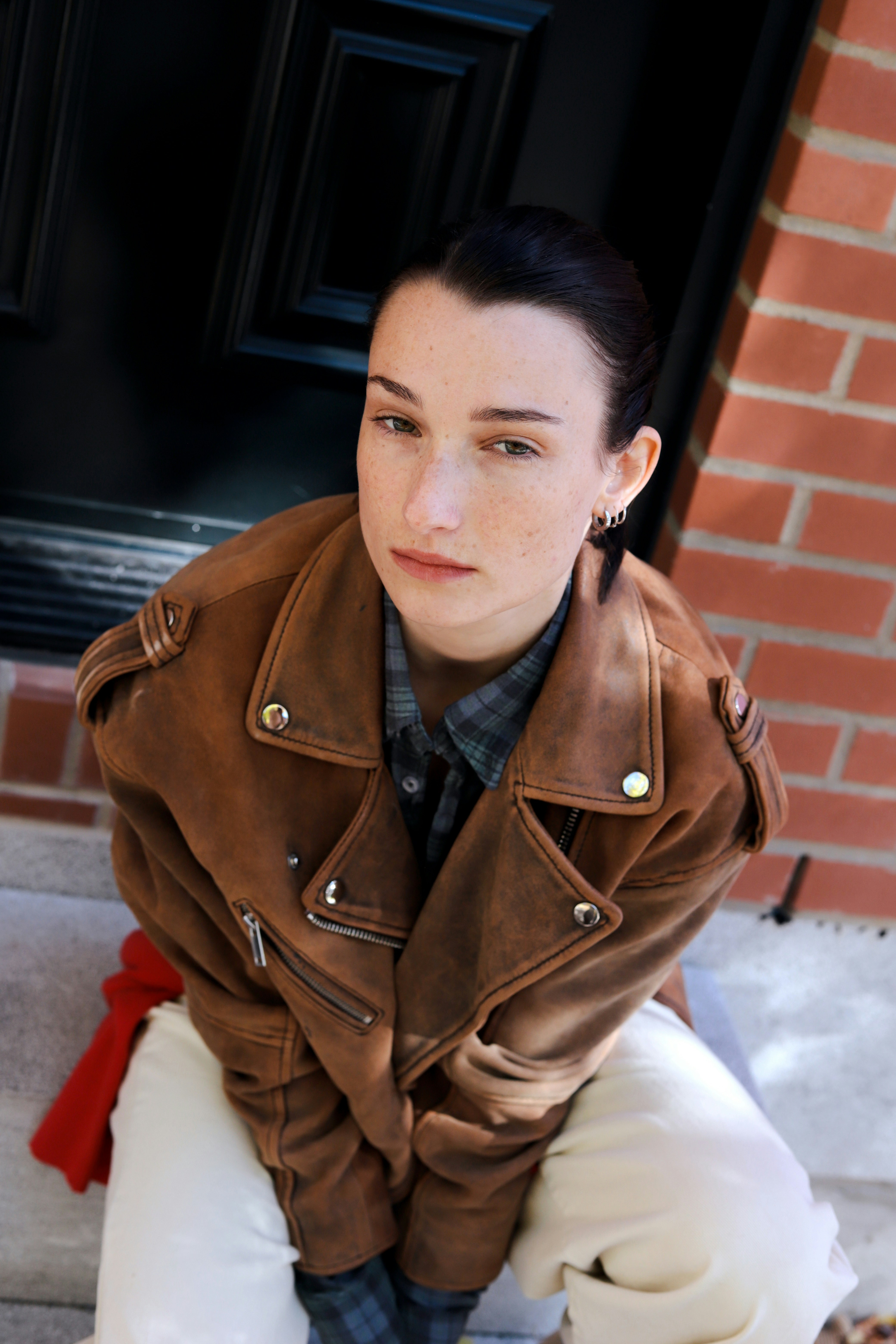 A person with dark hair in a brown leather jacket and white trousers sitting outdoors
