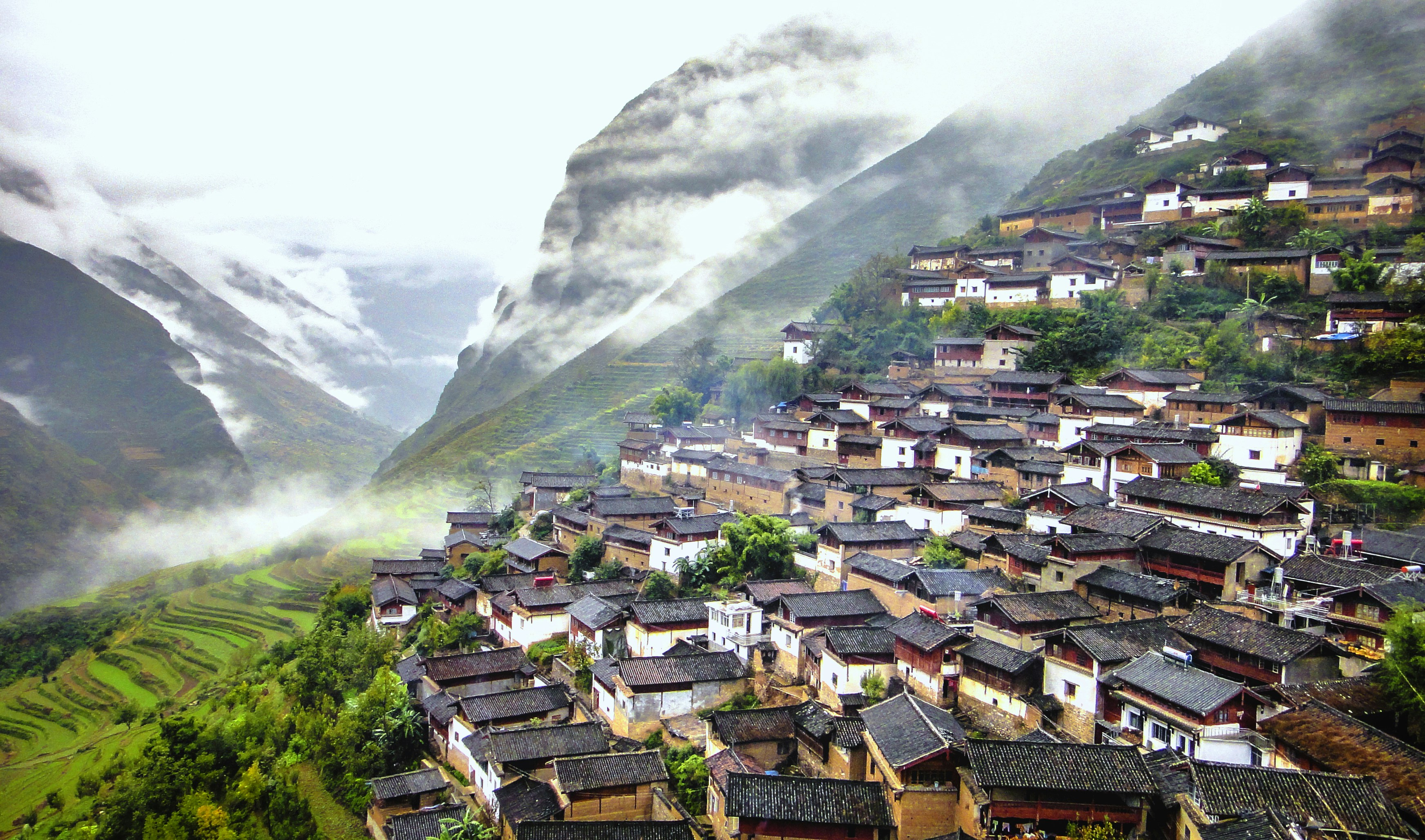 Illustrative photo: A village with traditional houses on a steep hillside above terraced fields and misty mountains