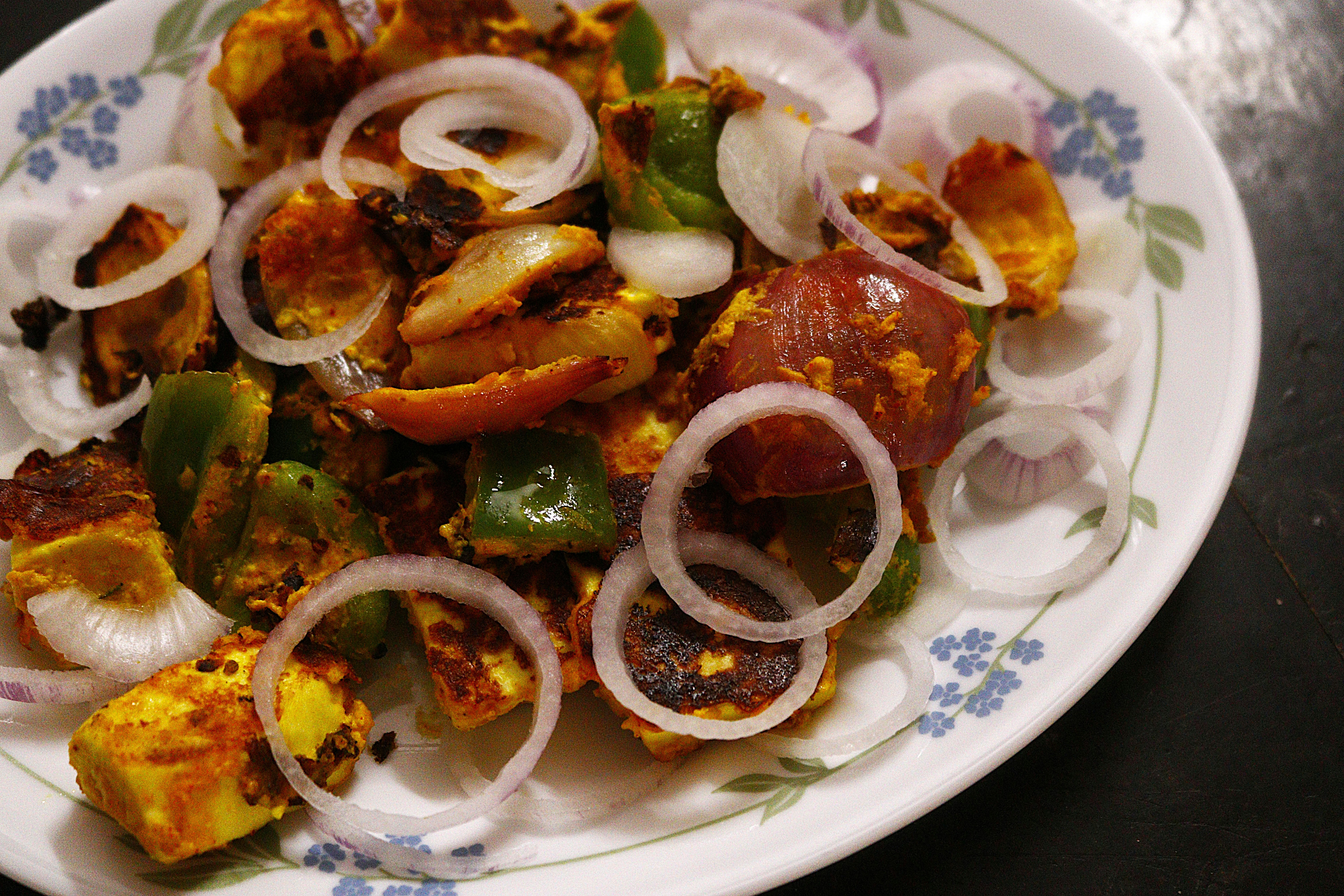 Paneer tikka with green bell peppers and raw onion rings on a floral plate