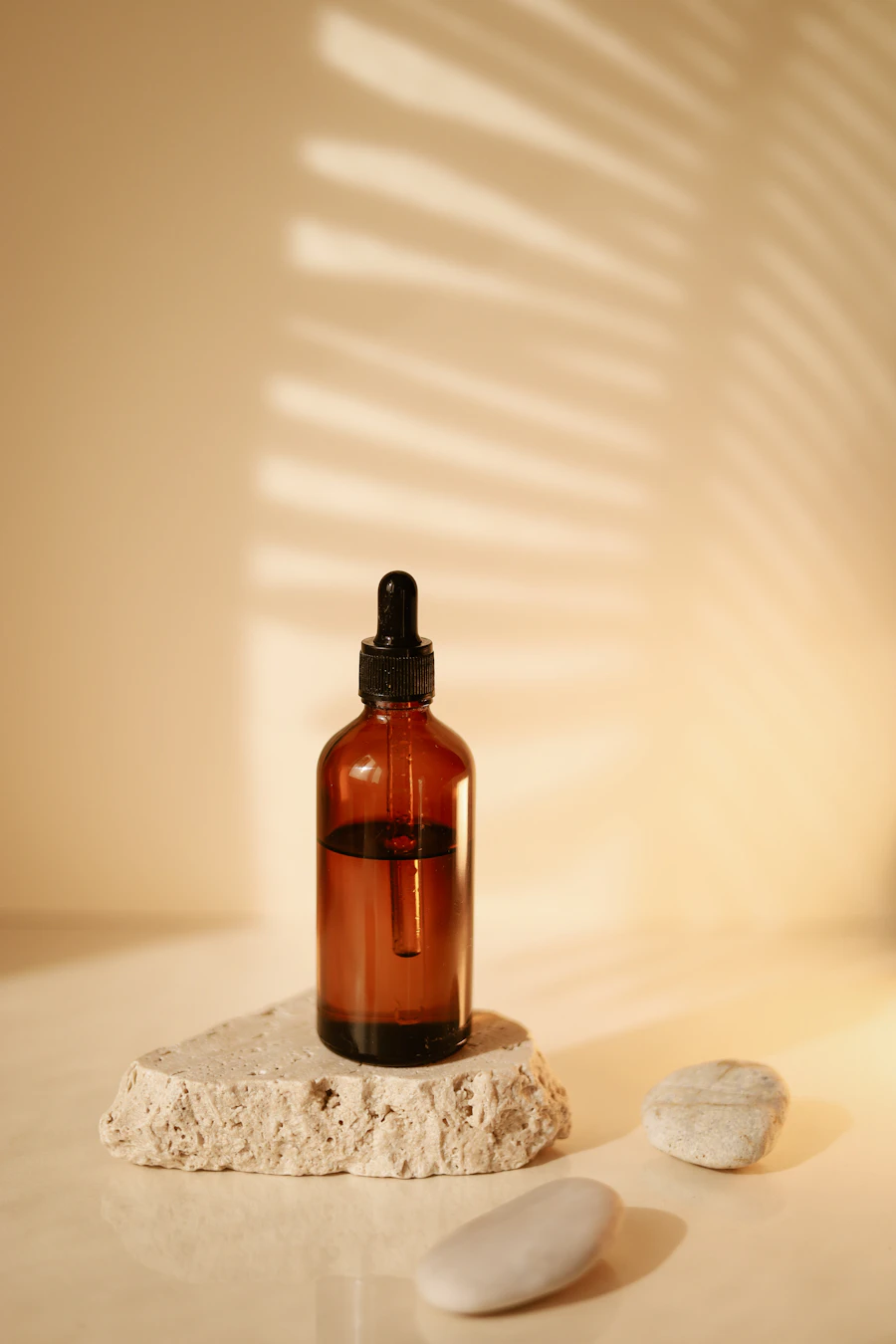 Amber dropper bottle on textured stone with palm-leaf shadows