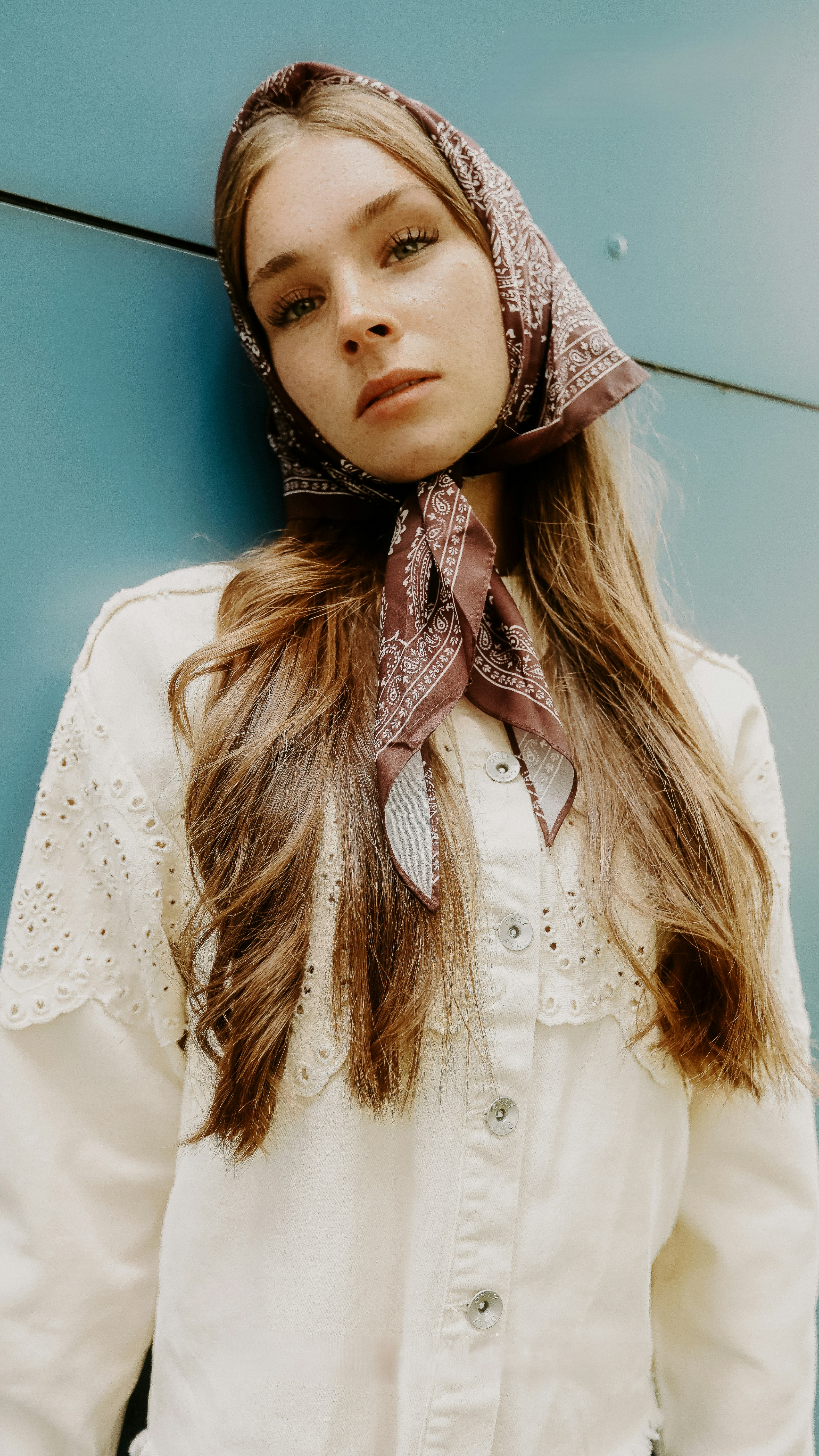 Retro Style Portrait with Patterned Headscarf Natural beauty portrait of a young woman leaning against a blue wall, wearing an elegant brown patterned headscarf and a textured cream shirt. - 相关推荐