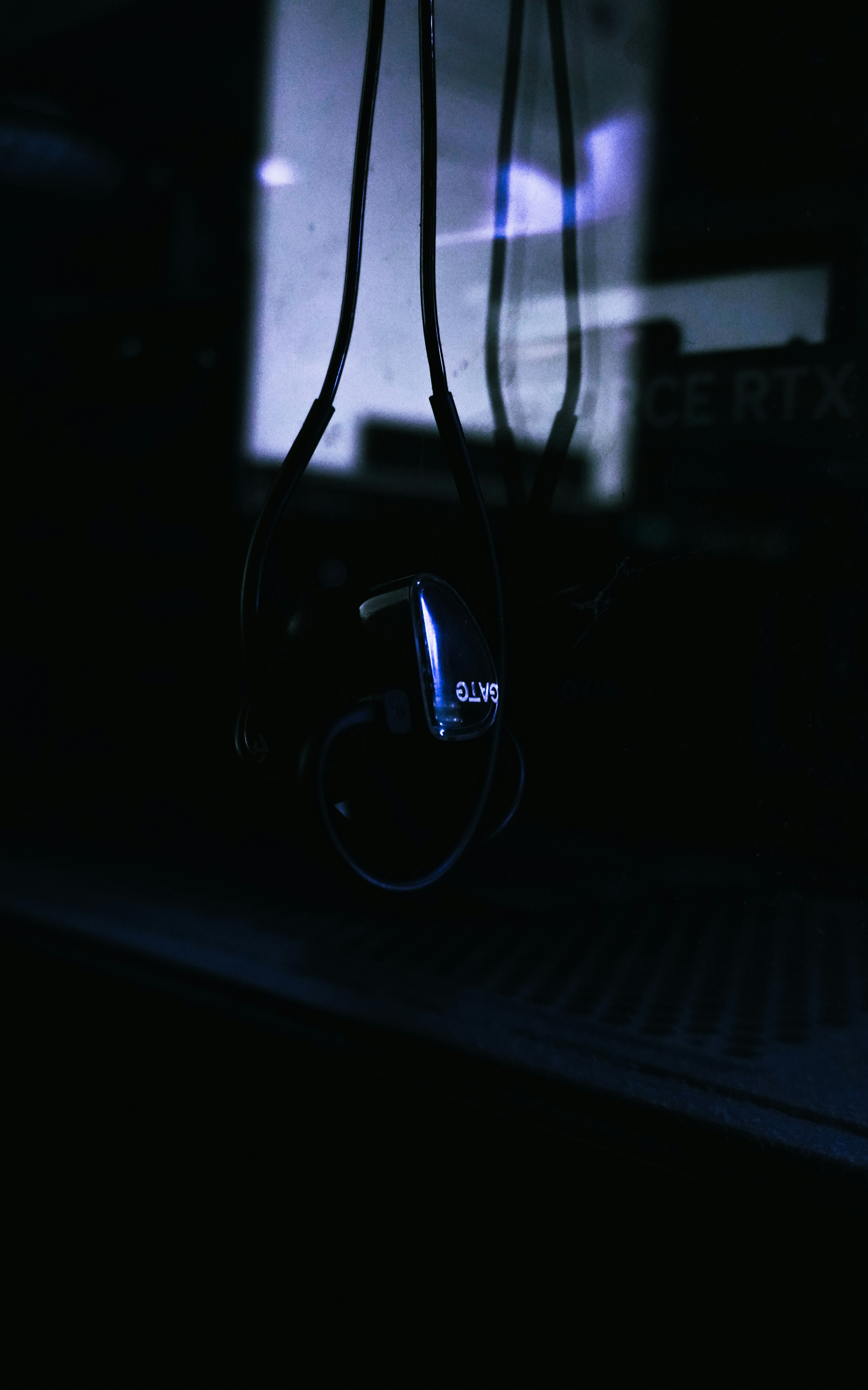 A pair of black wired earphones hanging in front of a dark computer case