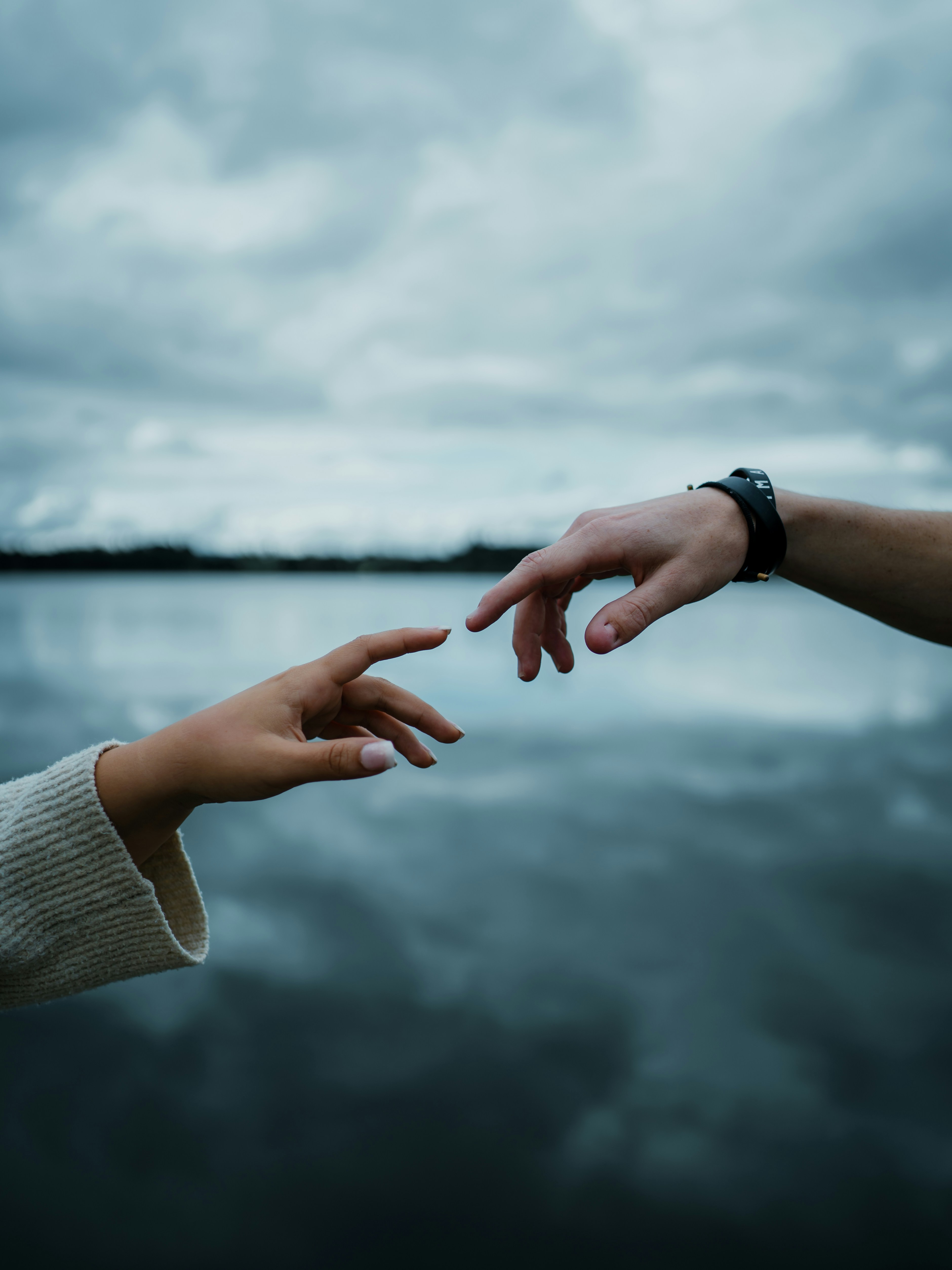 Two hands reaching toward each other against a blurred lake and cloudy sky - 相关推荐