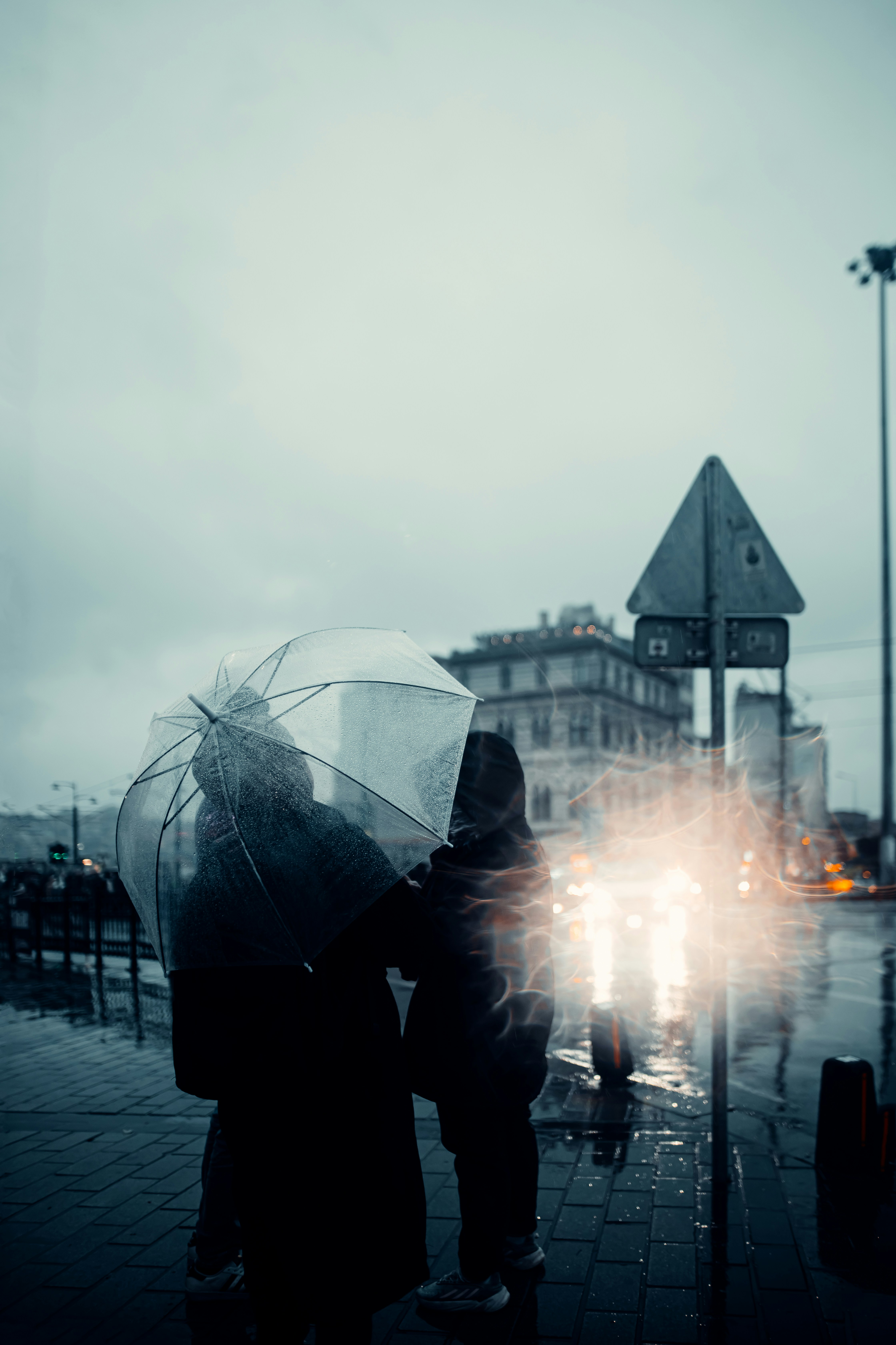 Two people under a clear umbrella on a rainy city street with blurred traffic lights - 相关推荐