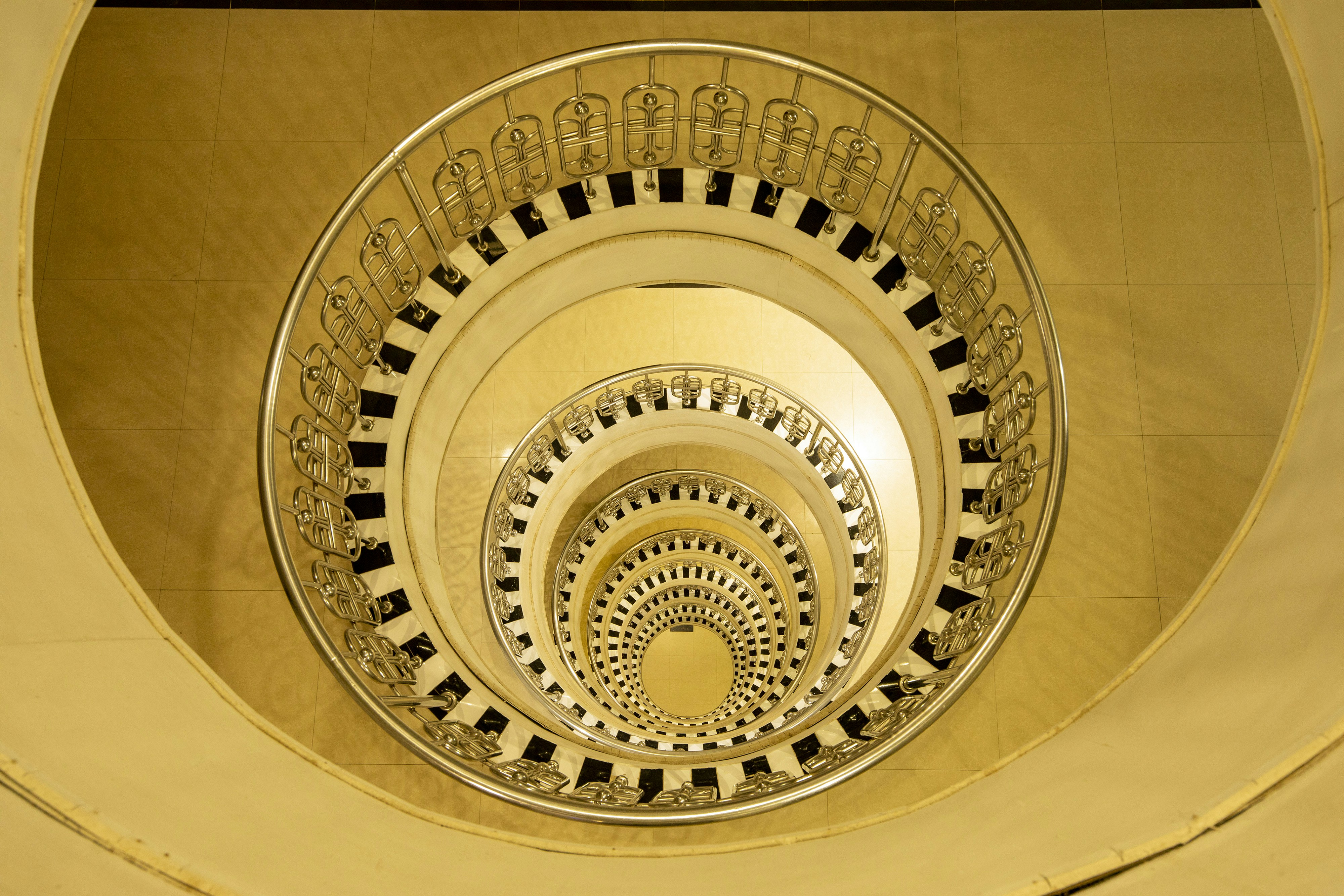 A high-angle view looking down a spiral staircase with black and white steps and metal railings - 相关推荐