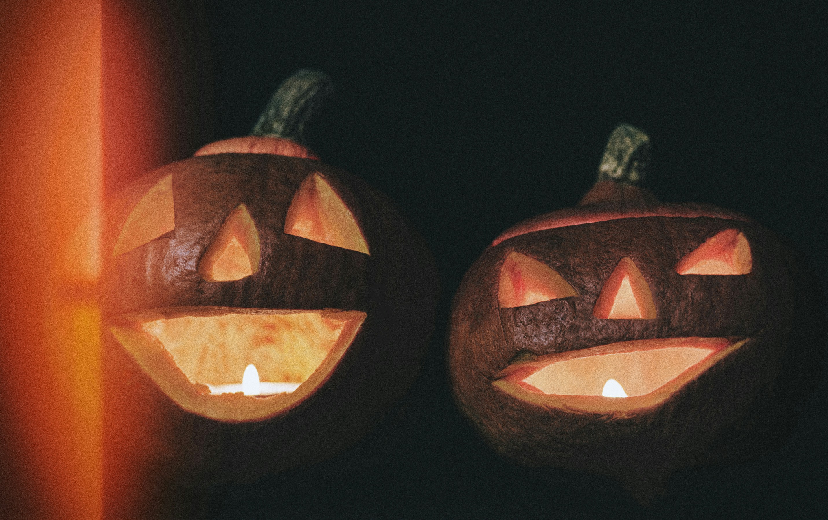 Two carved jack-o'-lanterns glowing with candlelight against a dark background in festive lighting - 相关推荐
