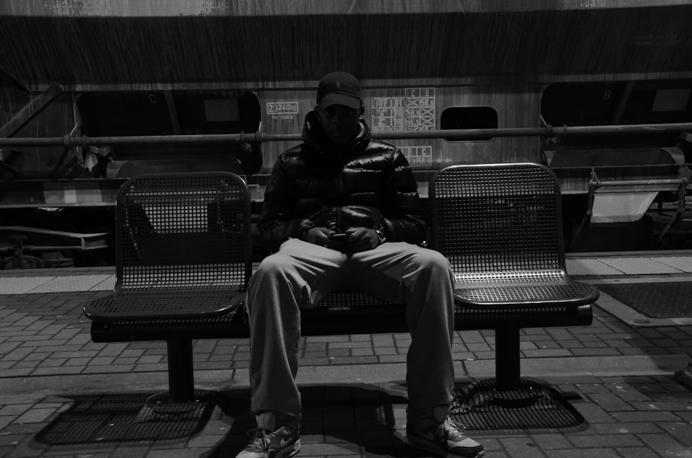 금속 벤치에 앉아있는 남자의 회색조 사진