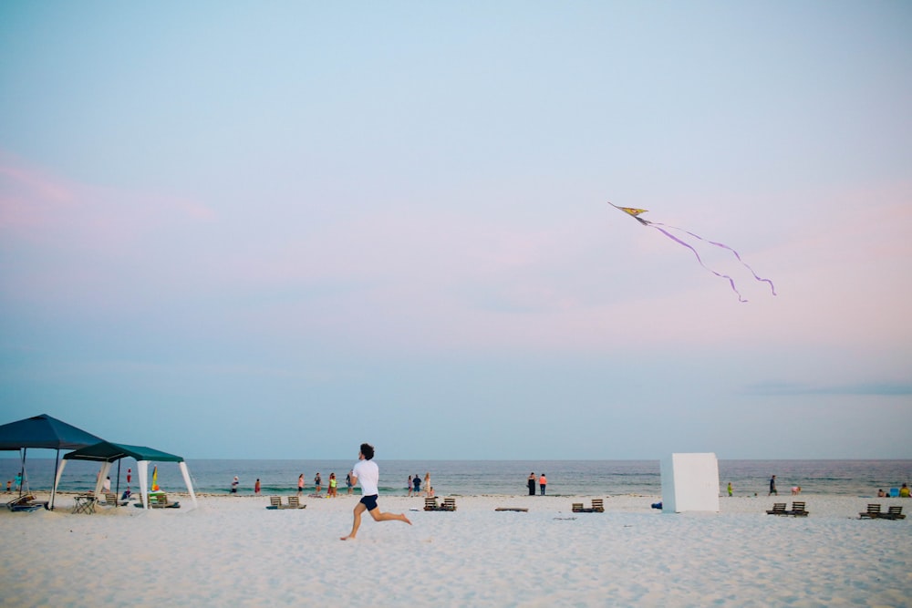 man running on white sand beach holding kite