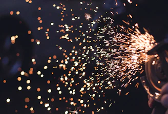 Dynamic shot of gas shielded welding sparks flying against a dark background with golden glow accents.