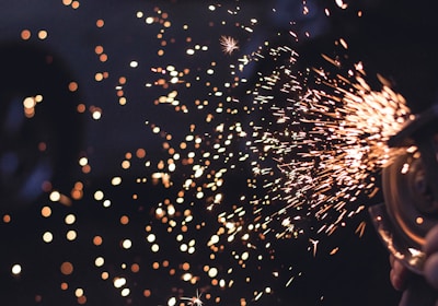 Macro shot of sparks flying from a copper surface, frozen mid-air against a black backdrop.