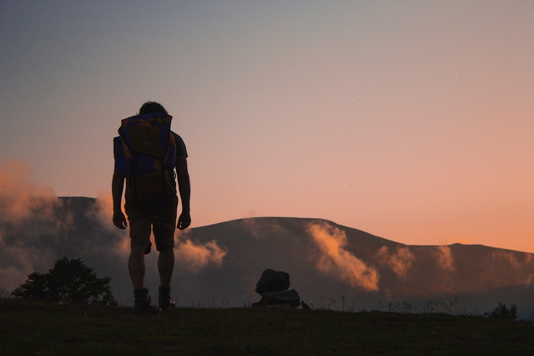 silhouette of man walking along field leading to mountain silhouette of man walking along field leading to mountain