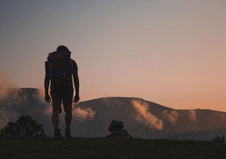 silhouette of man walking along field leading to mountain