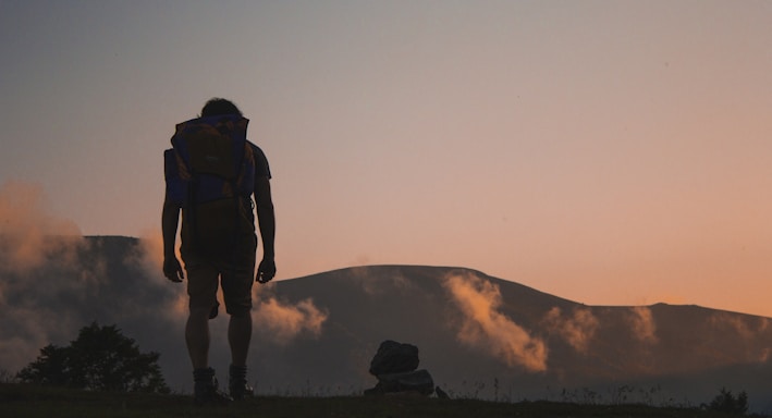 silhouette of man walking along field leading to mountain