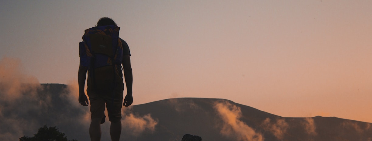 silhouette of man walking along field leading to mountain