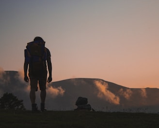 silhouette of man walking along field leading to mountain