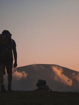 silhouette of man walking along field leading to mountain