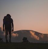 silhouette of man walking along field leading to mountain