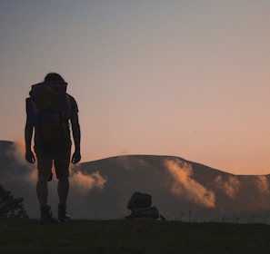 silhouette of man walking along field leading to mountain