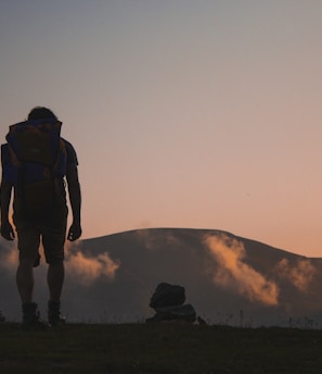 silhouette of man walking along field leading to mountain