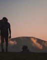 silhouette of man walking along field leading to mountain